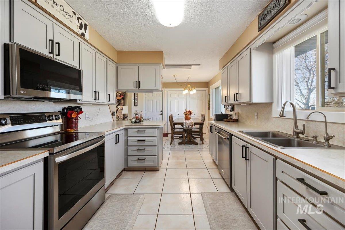 Kitchen with stainless steel appliances, gray cabinets, a chandelier, light countertops, and light tile patterned floors