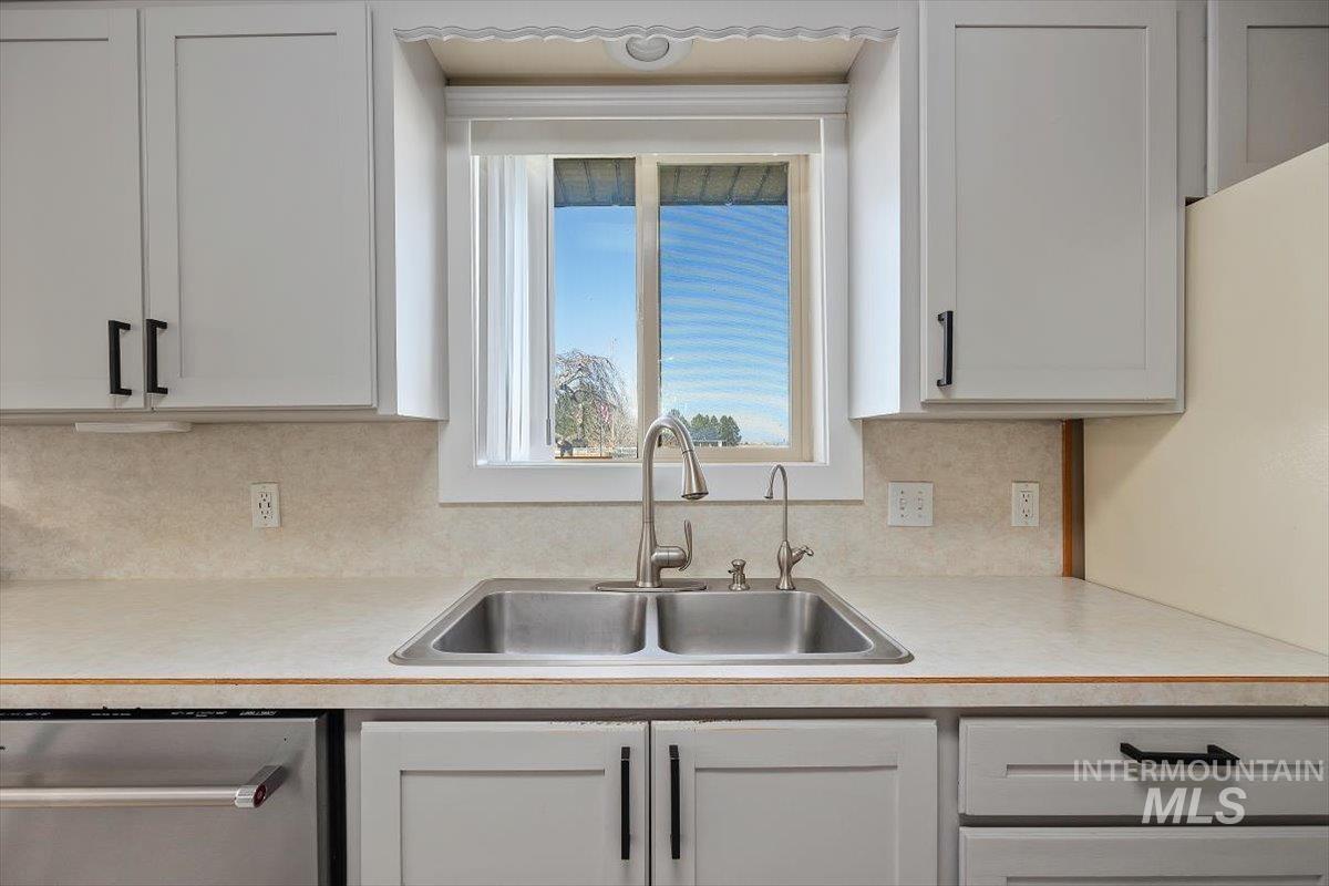 Kitchen with light countertops, stainless steel dishwasher, backsplash, and white cabinetry