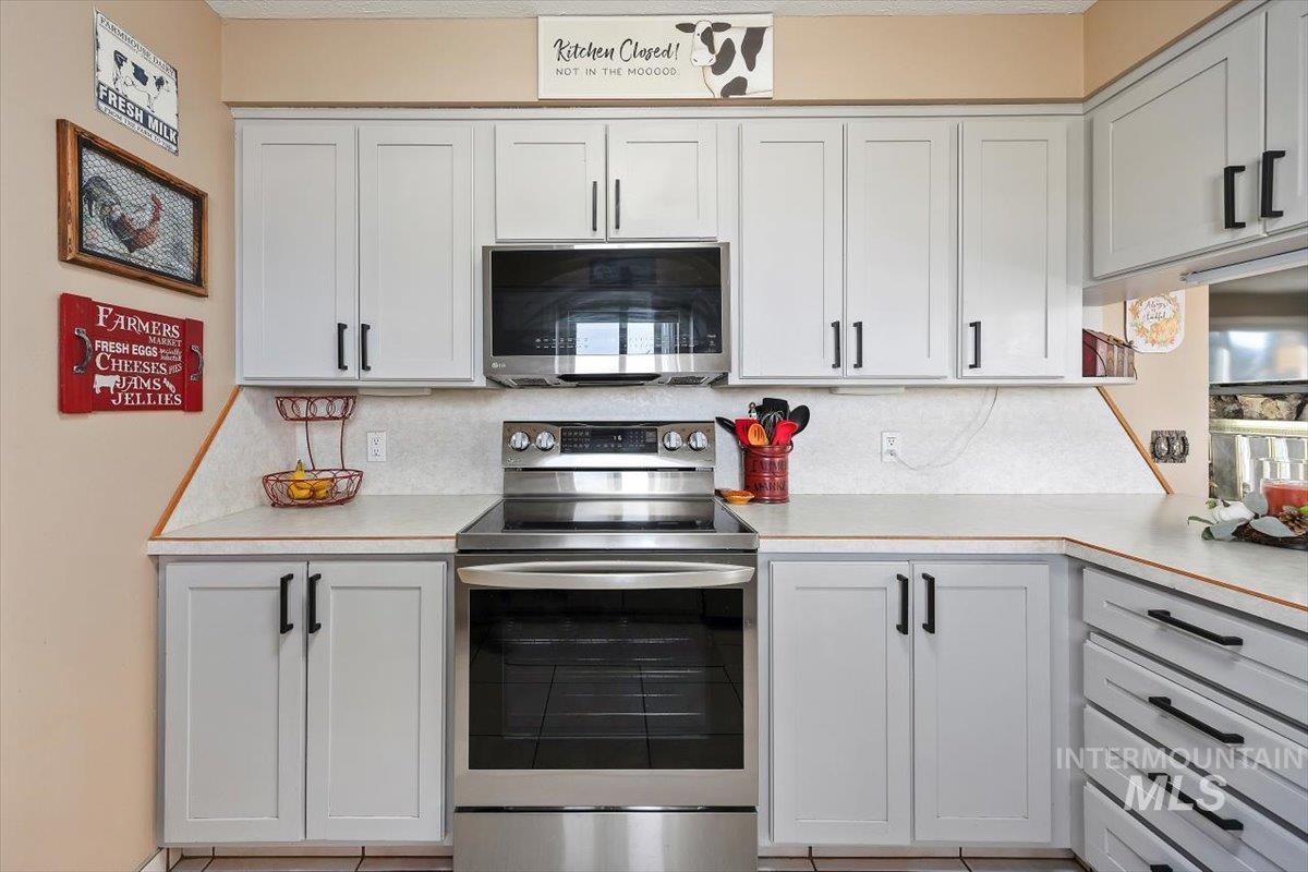 Kitchen with stainless steel appliances, light countertops, backsplash, and white cabinets
