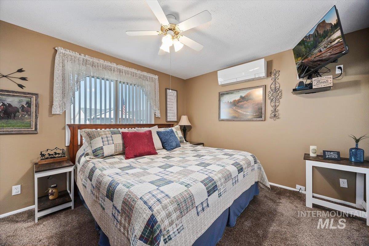 Bedroom featuring dark colored carpet, a ceiling fan, a textured ceiling, and a wall mounted AC