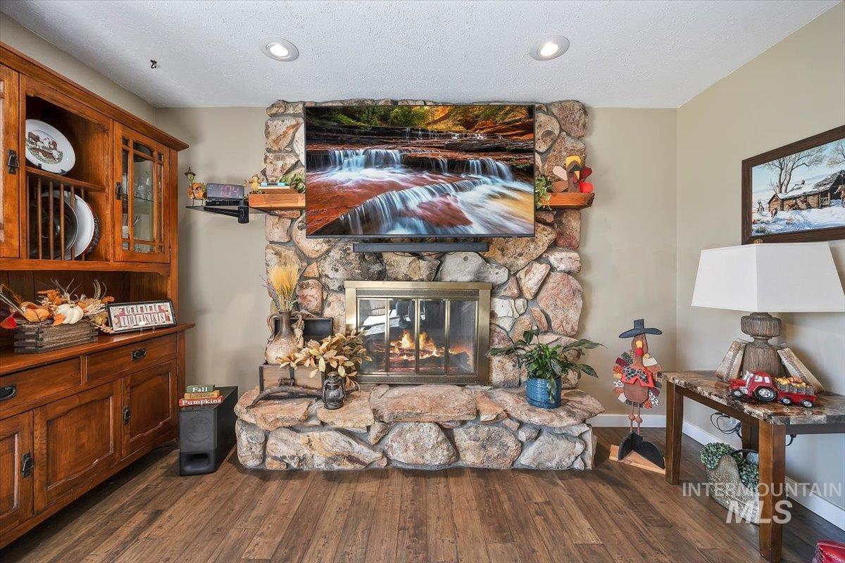 Living area with a stone fireplace, dark wood-style floors, a textured ceiling, and recessed lighting