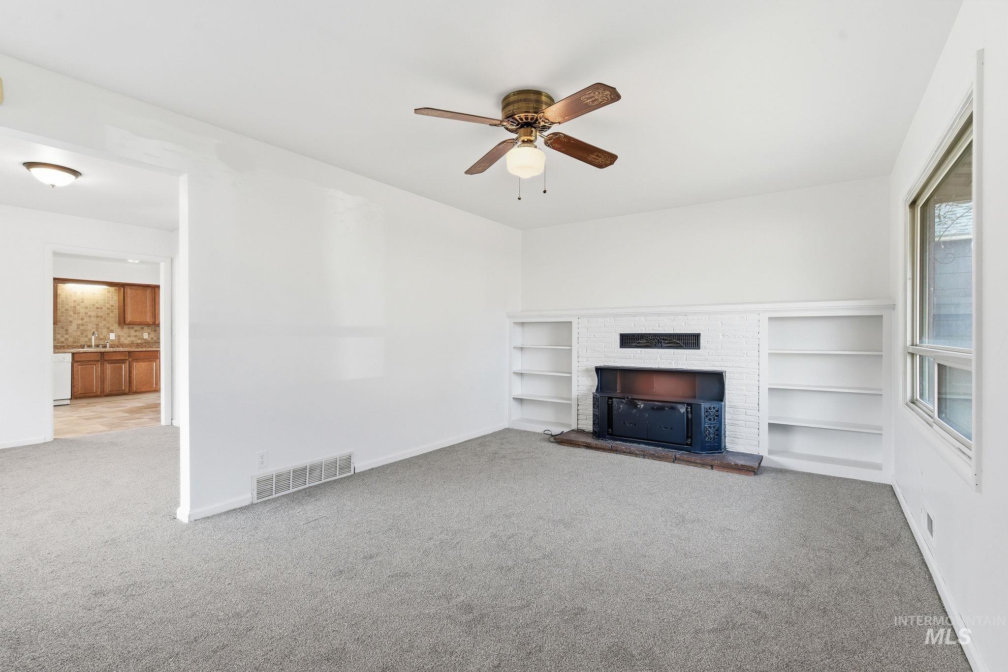 Unfurnished living room featuring a fireplace, light colored carpet, a ceiling fan, and built in features