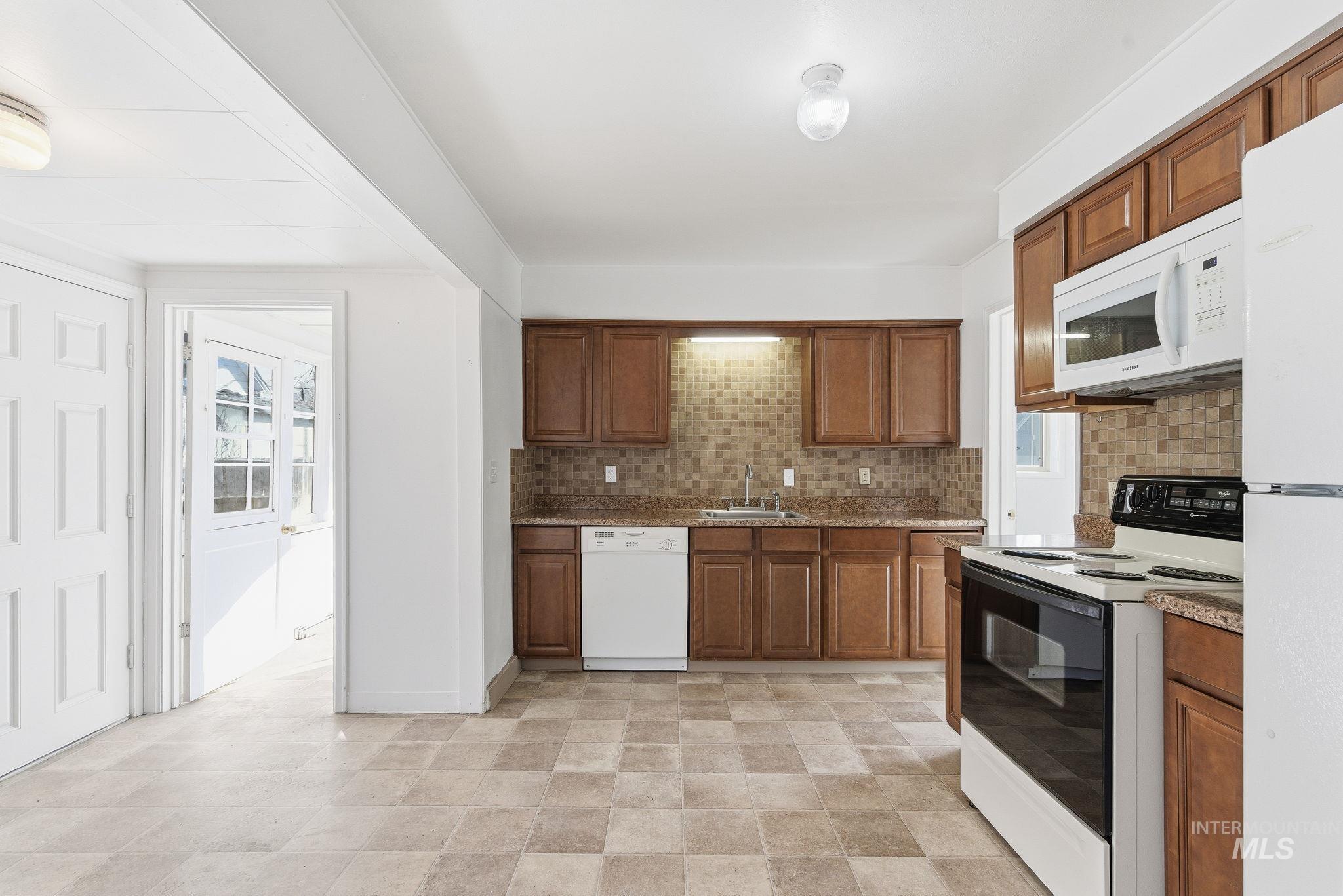 Kitchen with white appliances, brown cabinets, plenty of natural light, and backsplash