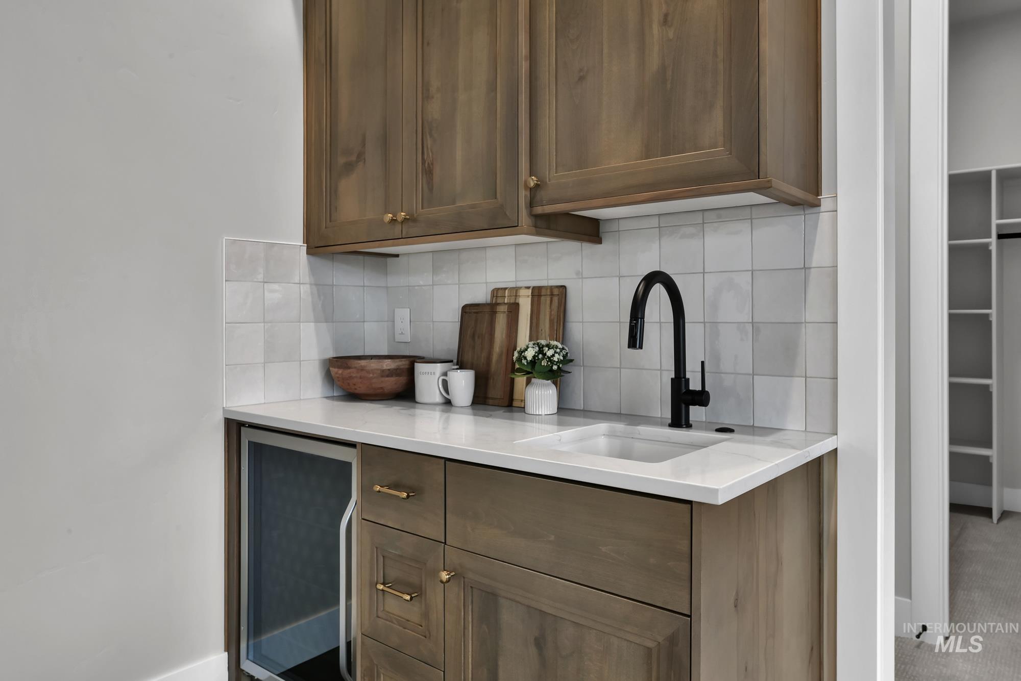 Bar area featuring beverage cooler, backsplash, and light stone countertops