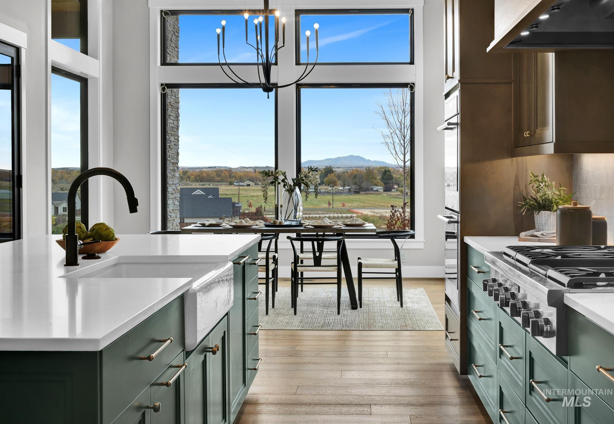 Kitchen featuring green cabinetry, hanging light fixtures, stainless steel appliances, ventilation hood, and light wood-type flooring