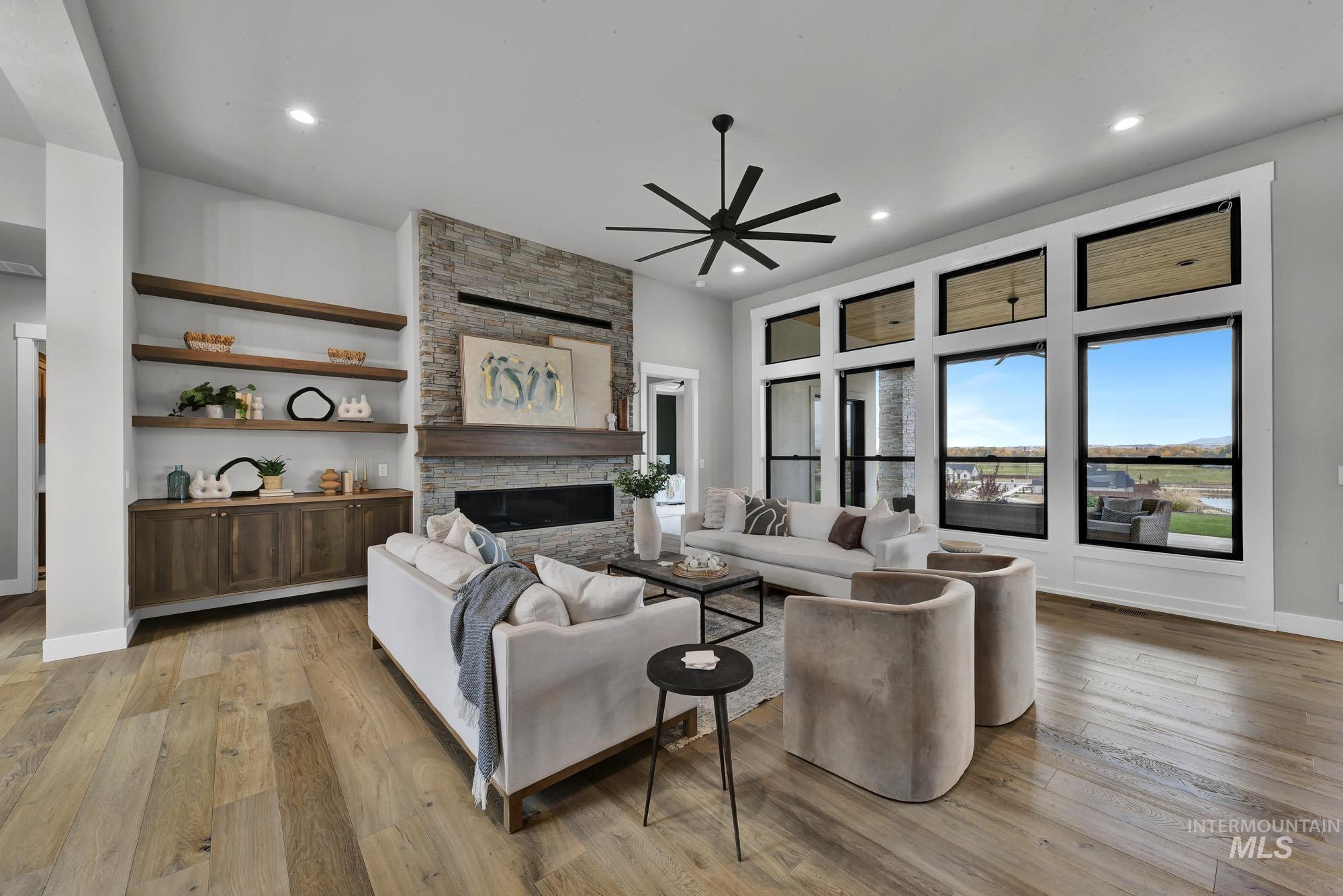 Living area featuring light wood finished floors, a stone fireplace, a ceiling fan, and recessed lighting
