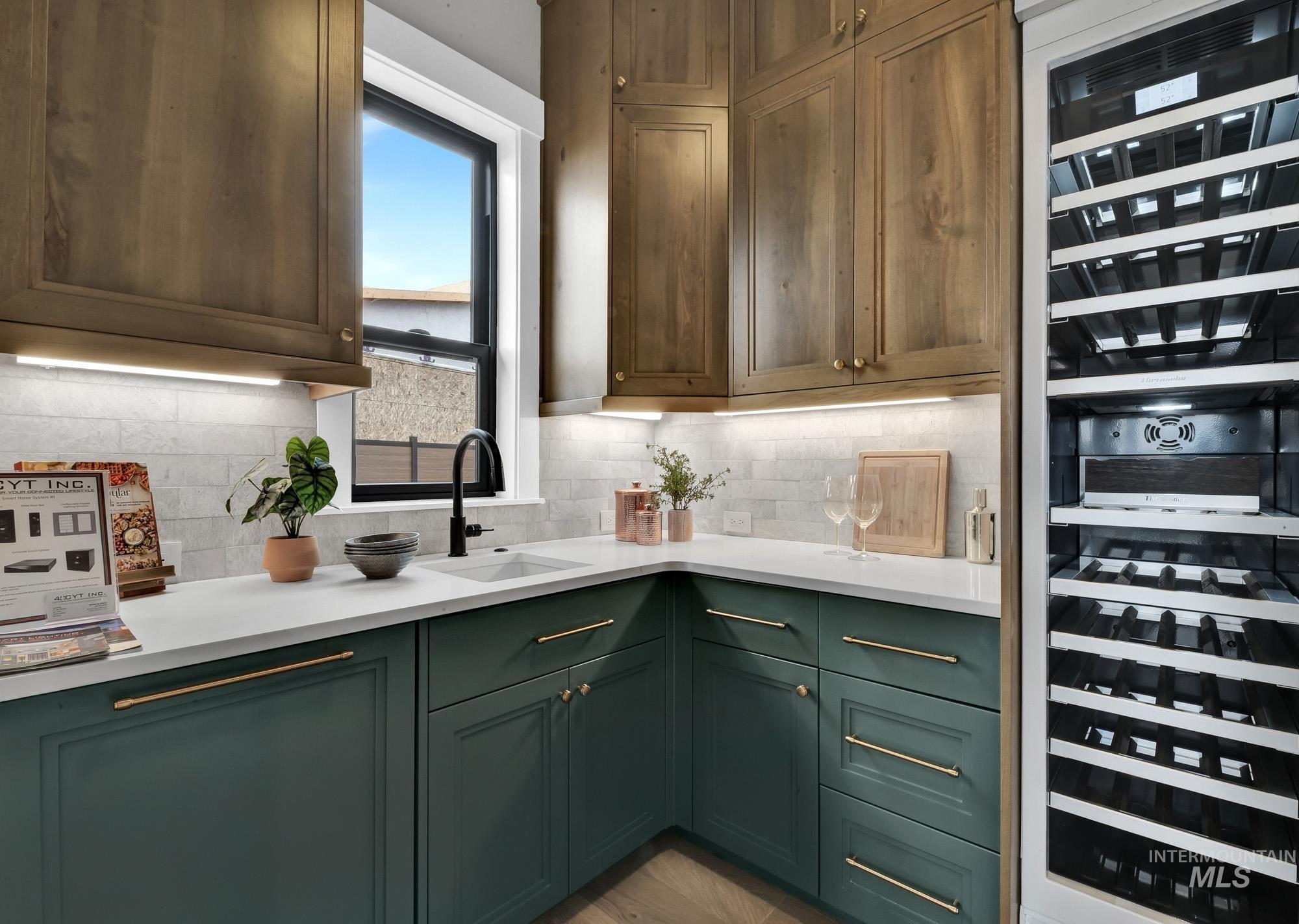 Kitchen with wine cooler, green cabinets, backsplash, and light stone countertops
