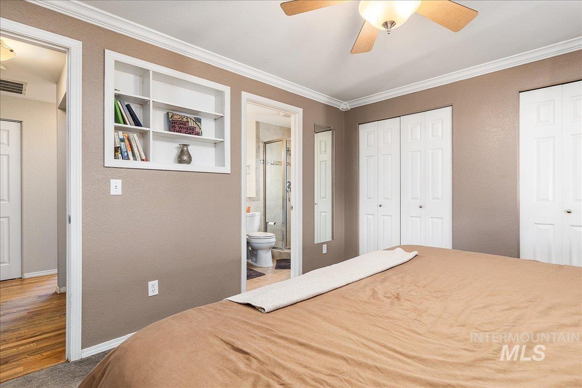 Bedroom with a textured wall, multiple closets, ornamental molding, ensuite bath, and ceiling fan