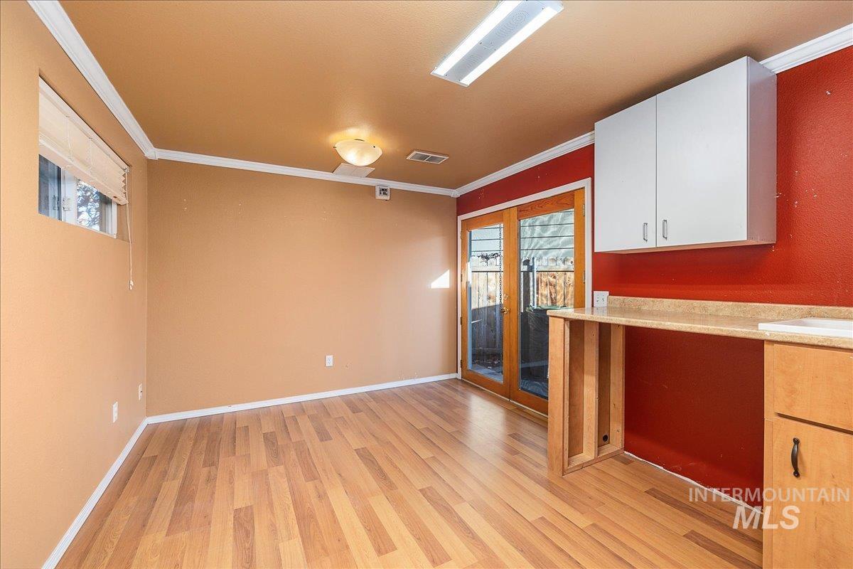 Kitchen featuring crown molding, white cabinetry, french doors, light wood-style flooring, and light stone countertops