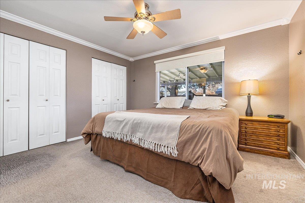 Carpeted bedroom featuring two closets, crown molding, ceiling fan, and a textured wall