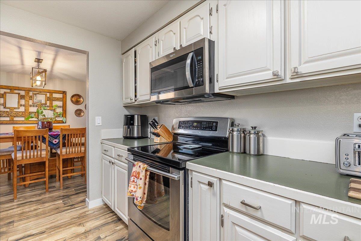 Kitchen featuring stainless steel appliances, white cabinets, light wood-style flooring, and light countertops