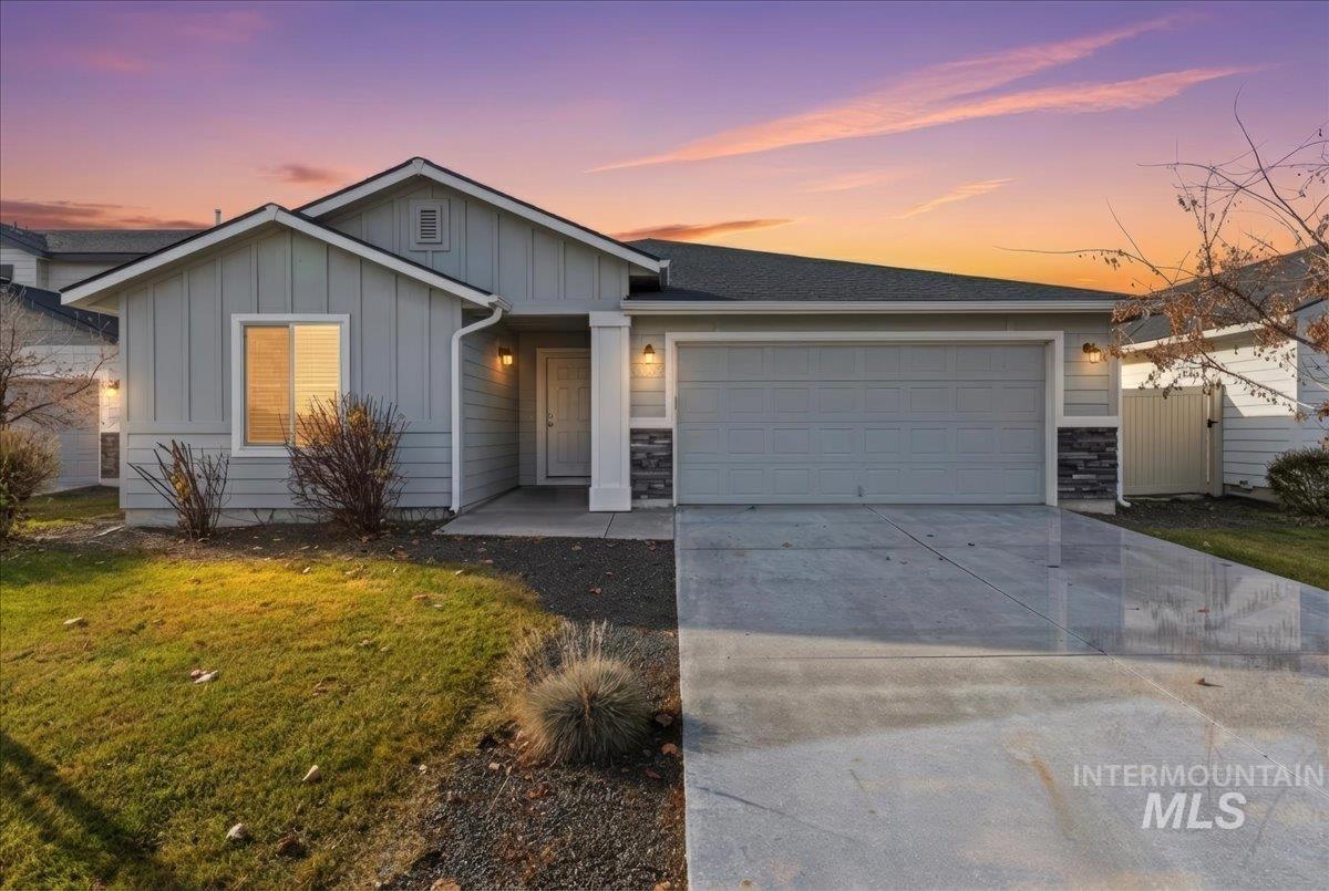 Single story home with board and batten siding, driveway, stone siding, a garage, and a lawn