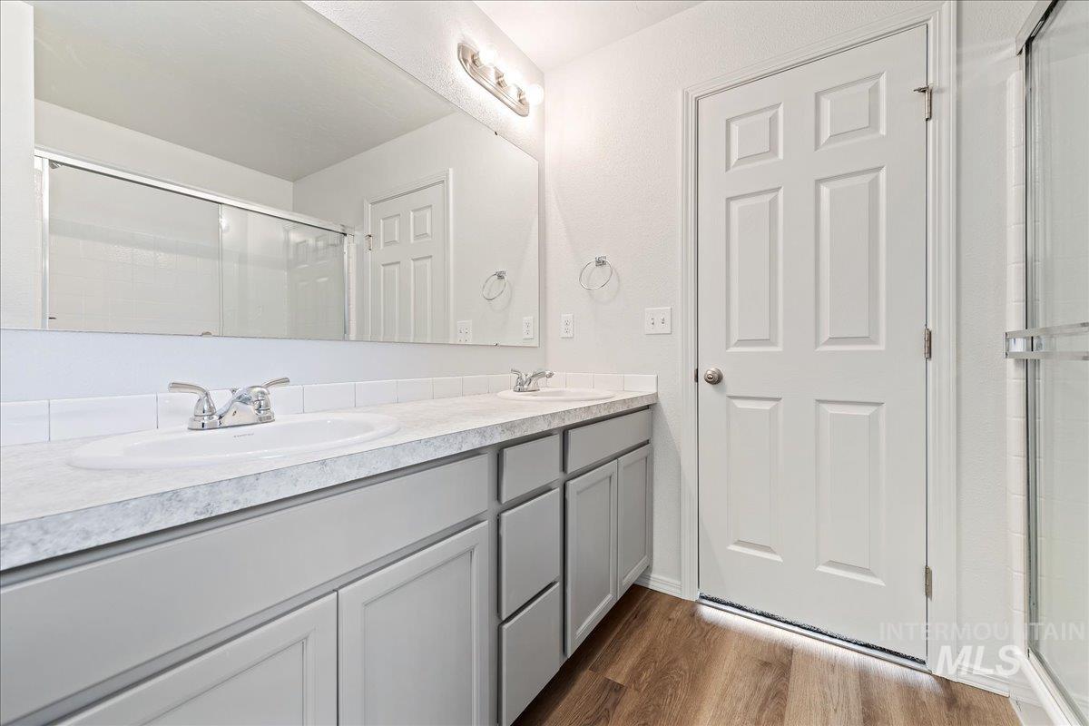 Full bath with a stall shower, double vanity, and dark wood-style flooring