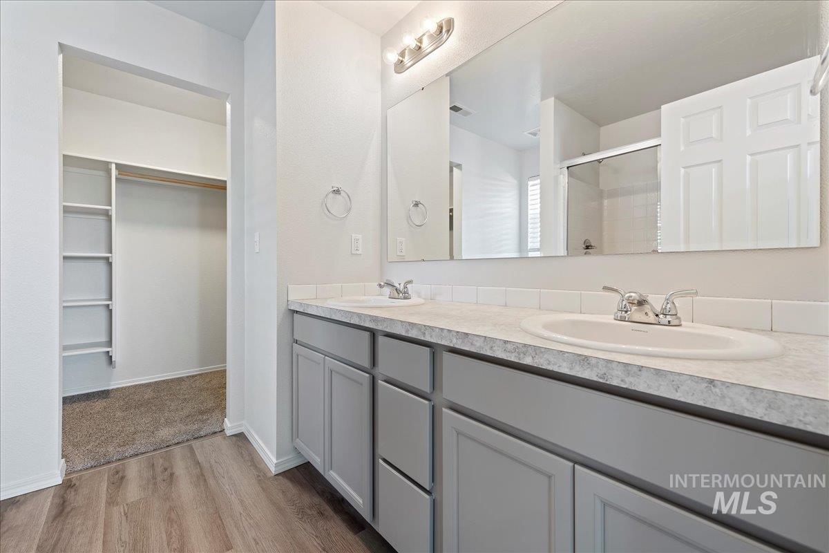 Full bathroom featuring a spacious closet, double vanity, a shower stall, and light wood-style floors
