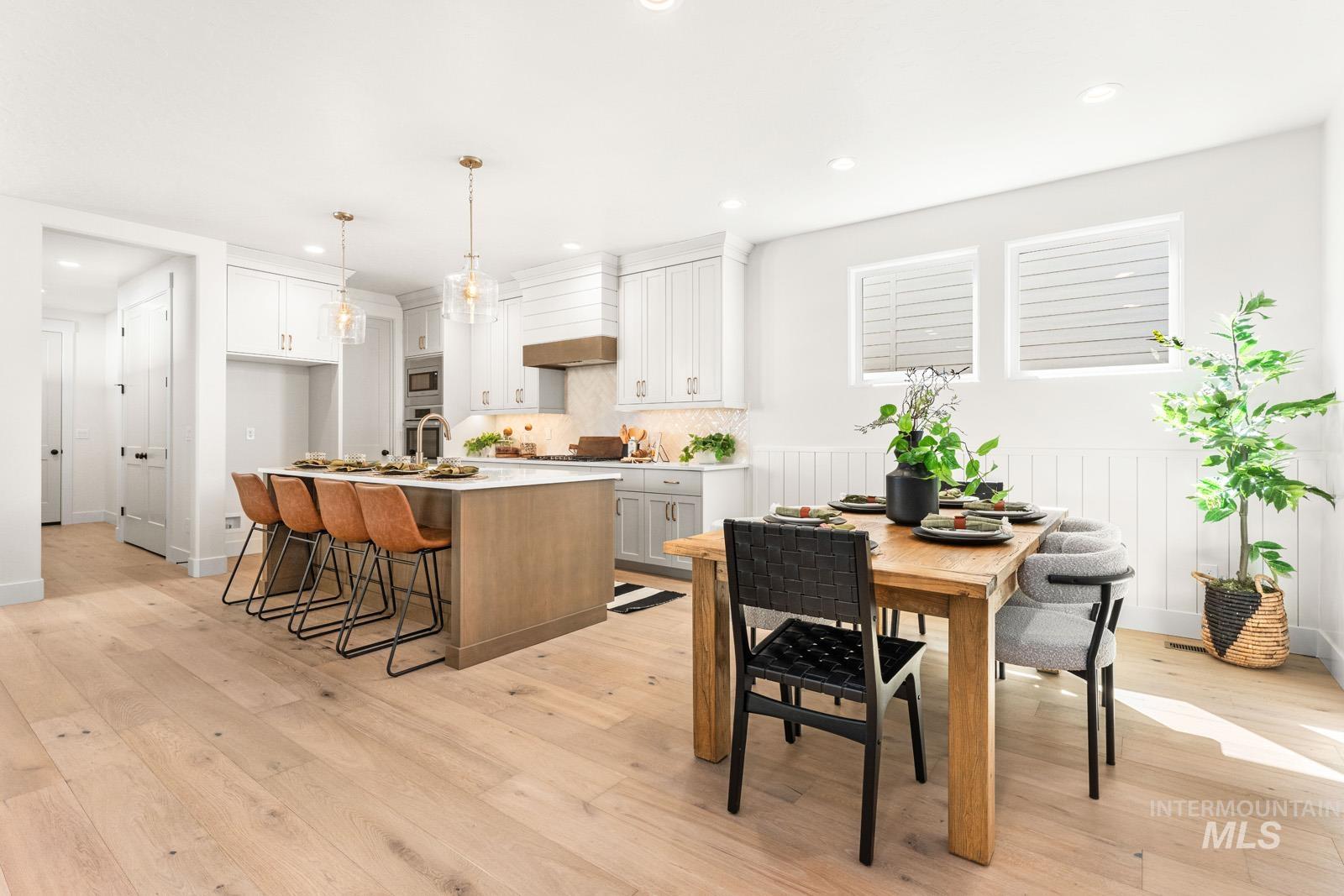 Kitchen featuring two tone cabinetry, an island with sink, light wood finished floors, a kitchen bar, and stainless steel appliances