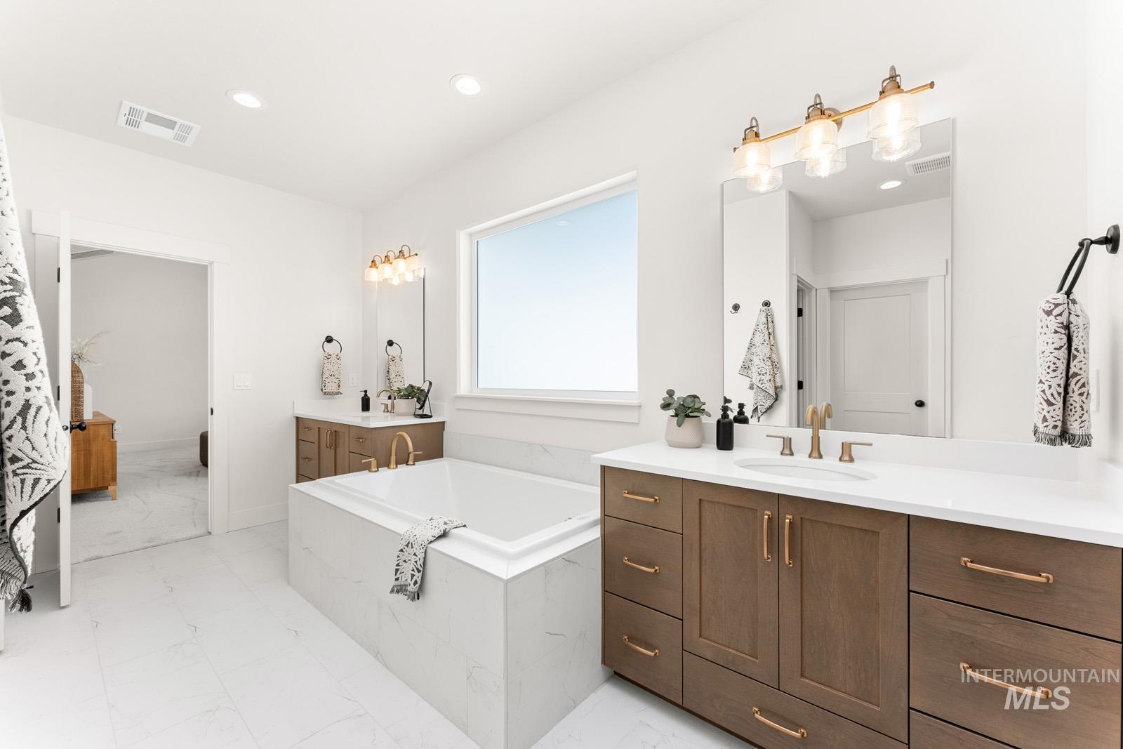Bathroom with two vanities, a bath, recessed lighting, and light marble finish flooring