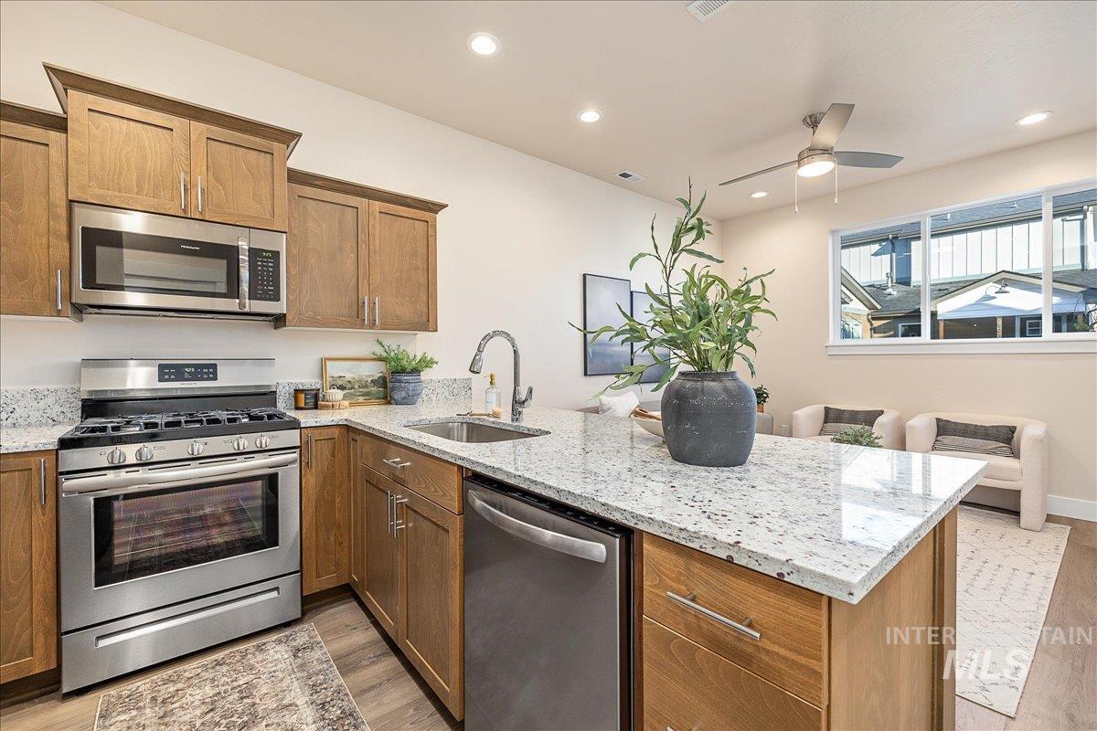 Kitchen with appliances with stainless steel finishes, light stone countertops, brown cabinetry, and recessed lighting