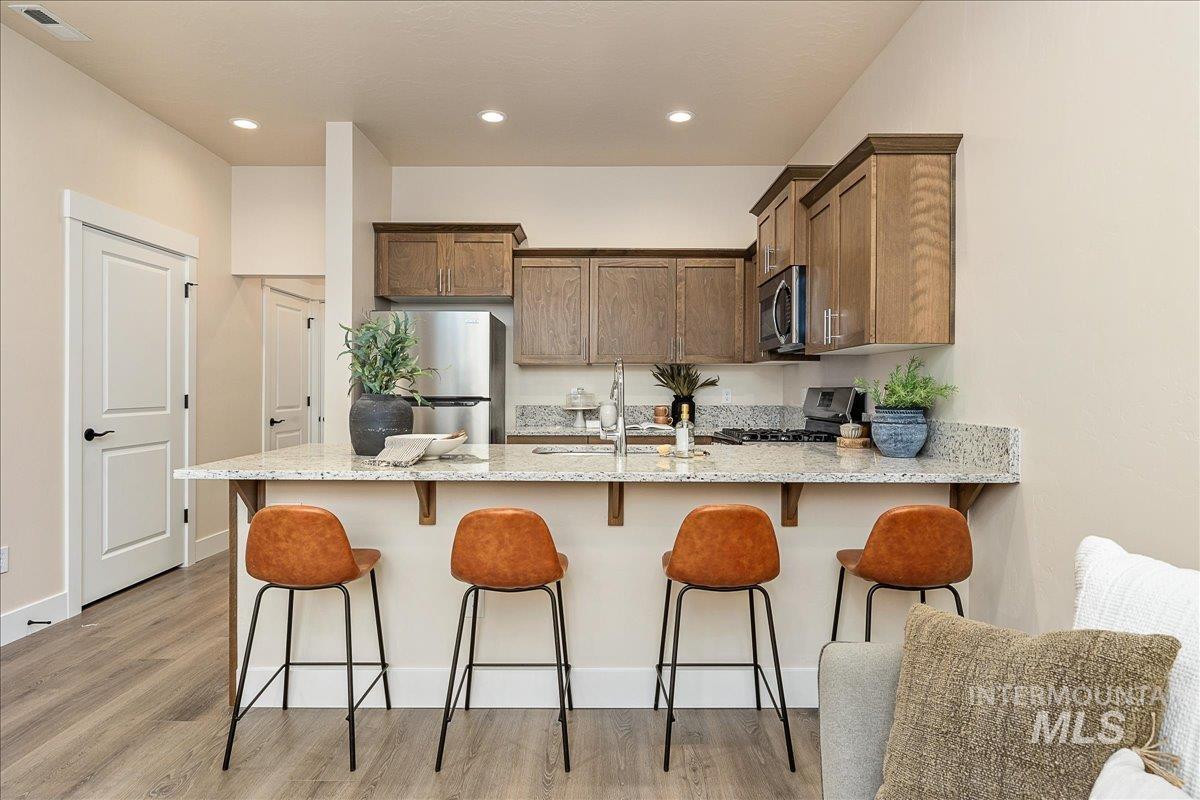Kitchen with a peninsula, light stone counters, a breakfast bar area, appliances with stainless steel finishes, and light wood-style floors