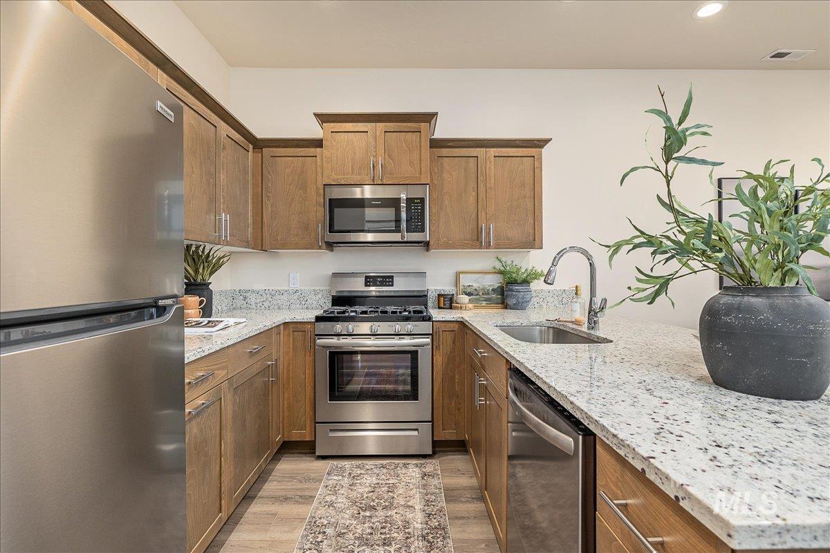Kitchen with appliances with stainless steel finishes, light stone countertops, brown cabinets, light wood-style flooring, and a peninsula