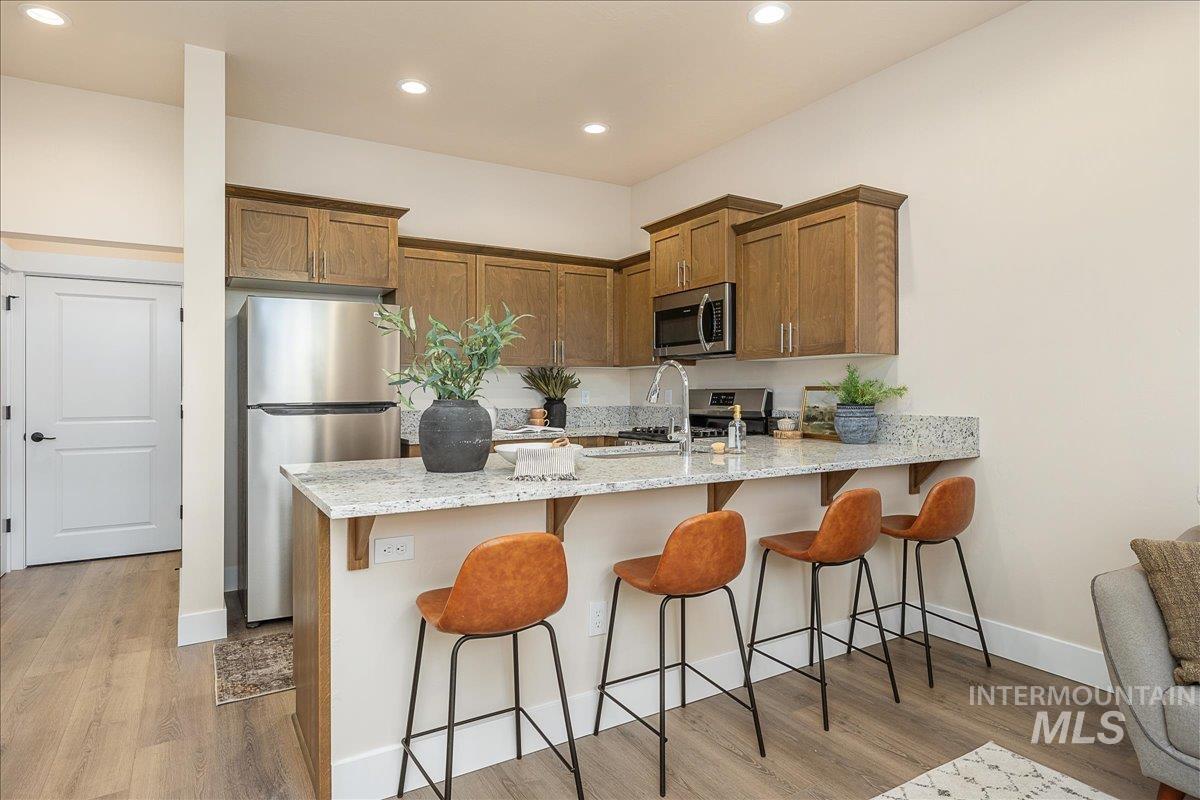 Kitchen with a kitchen breakfast bar, light stone countertops, stainless steel appliances, brown cabinets, and a peninsula