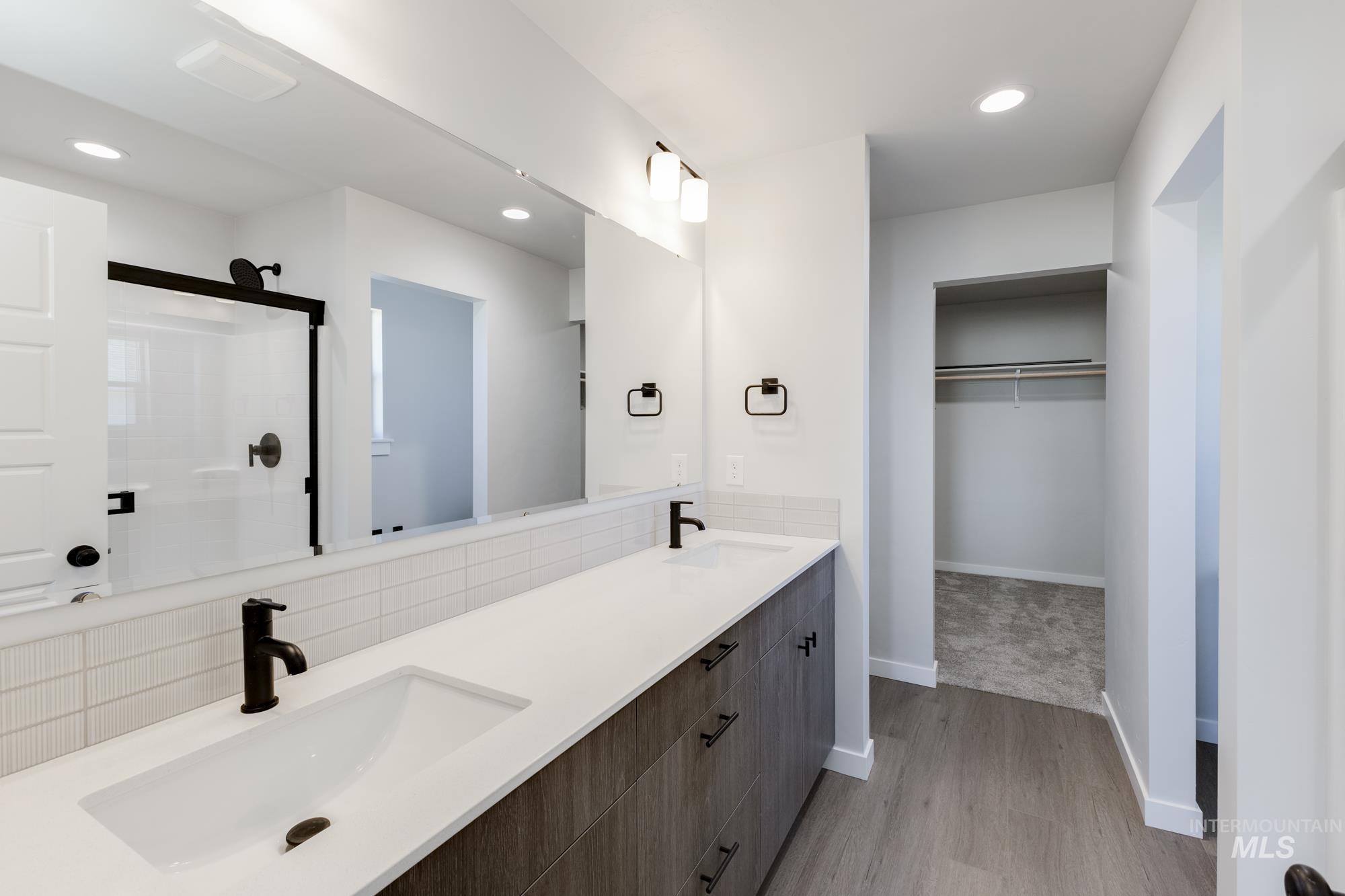 Full bathroom with a walk in closet, a stall shower, double vanity, tasteful backsplash, and light wood finished floors