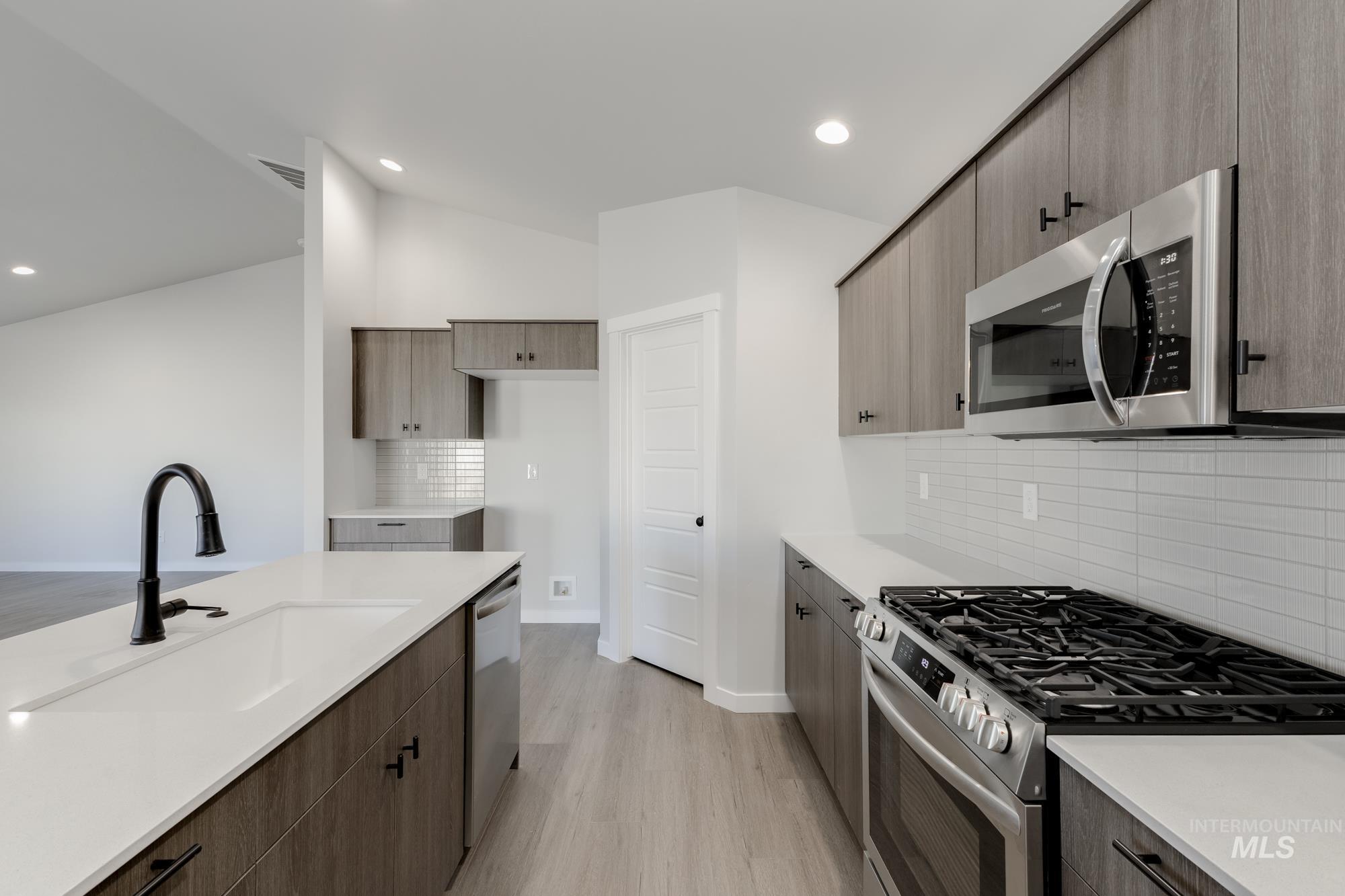 Kitchen featuring stainless steel appliances, decorative backsplash, modern cabinets, light wood finished floors, and recessed lighting