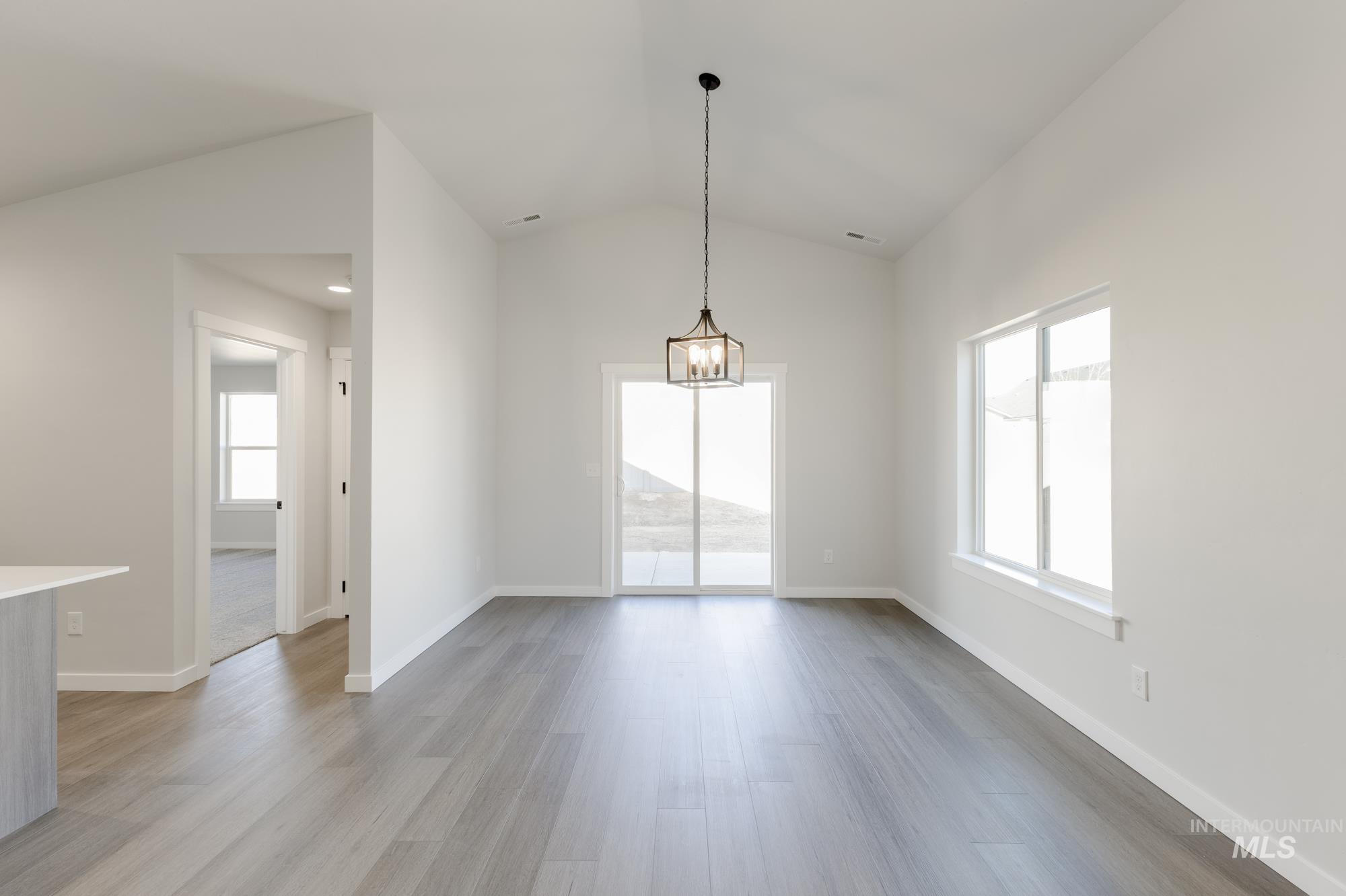 Unfurnished dining area with lofted ceiling, light wood-type flooring, and a chandelier