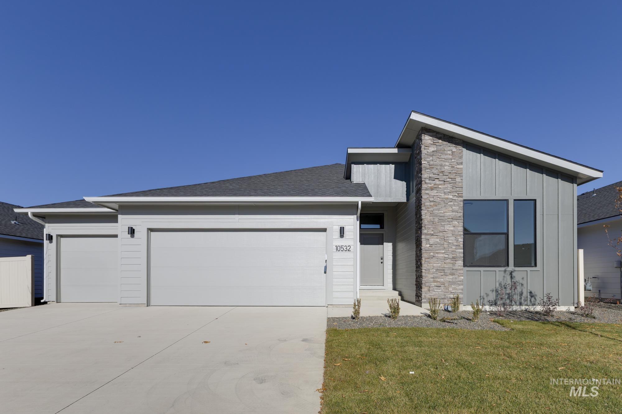 View of front of property with board and batten siding, a garage, driveway, stone siding, and a front yard