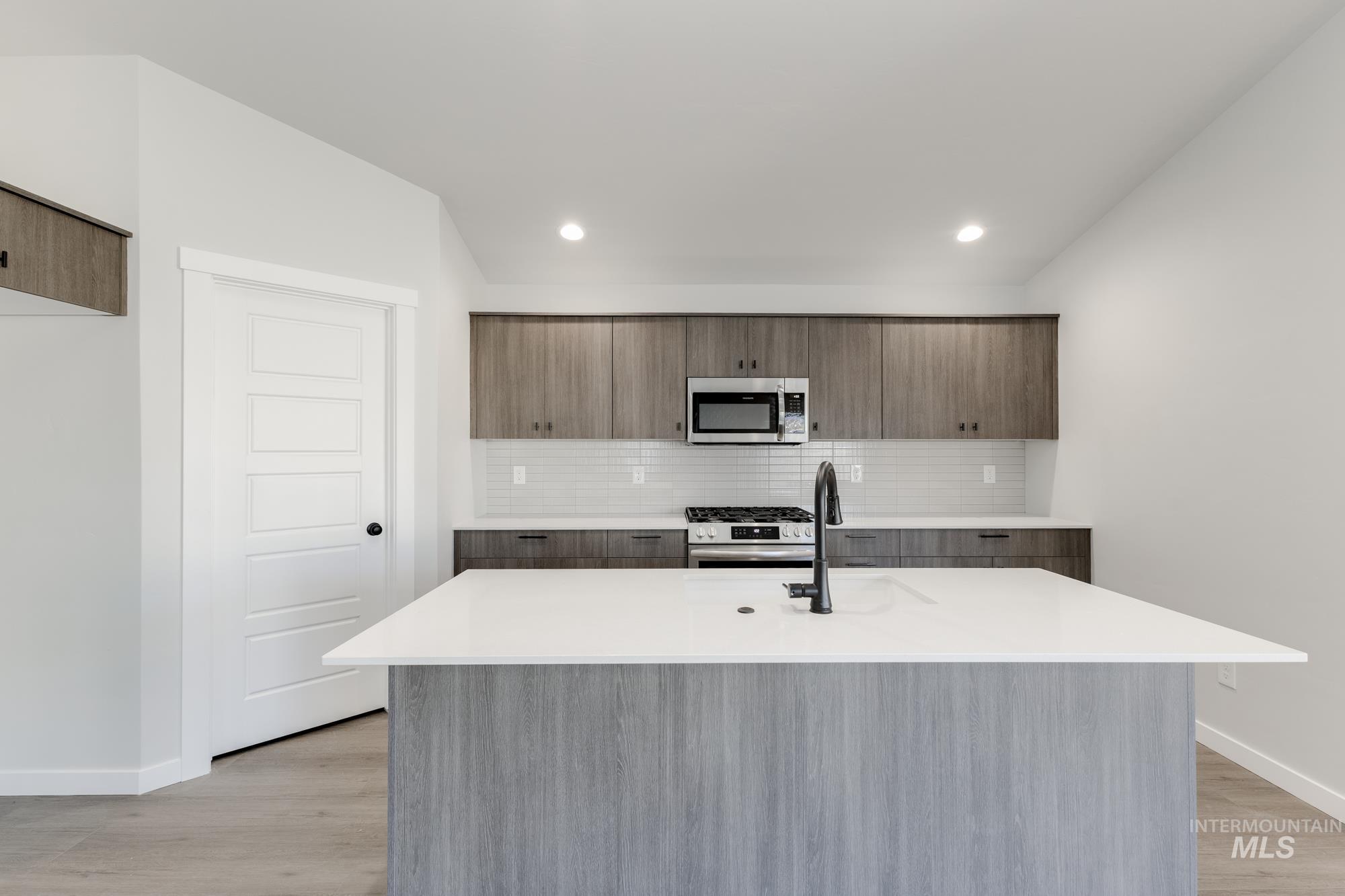 Kitchen featuring tasteful backsplash, modern cabinets, stainless steel appliances, a center island with sink, and light stone countertops
