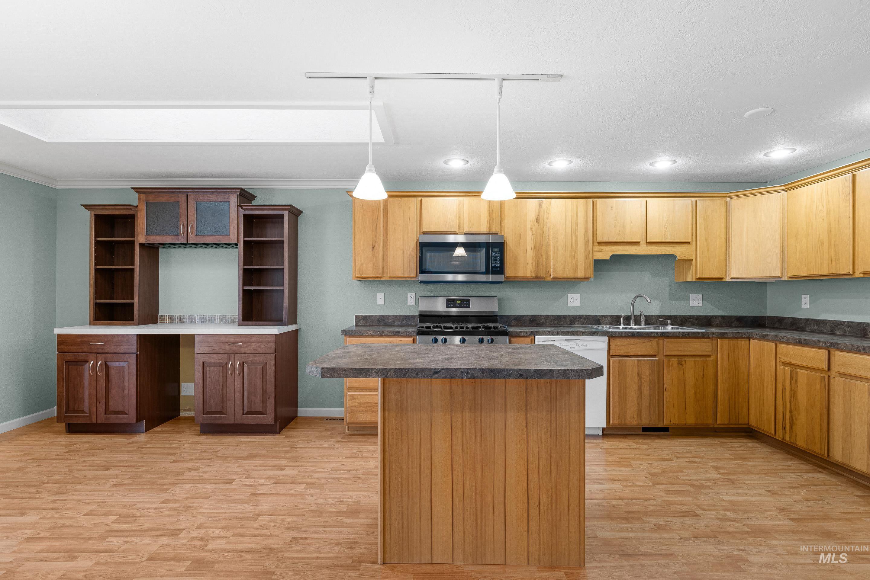 Kitchen with dark countertops, a center island, stainless steel appliances, and light wood-style floors