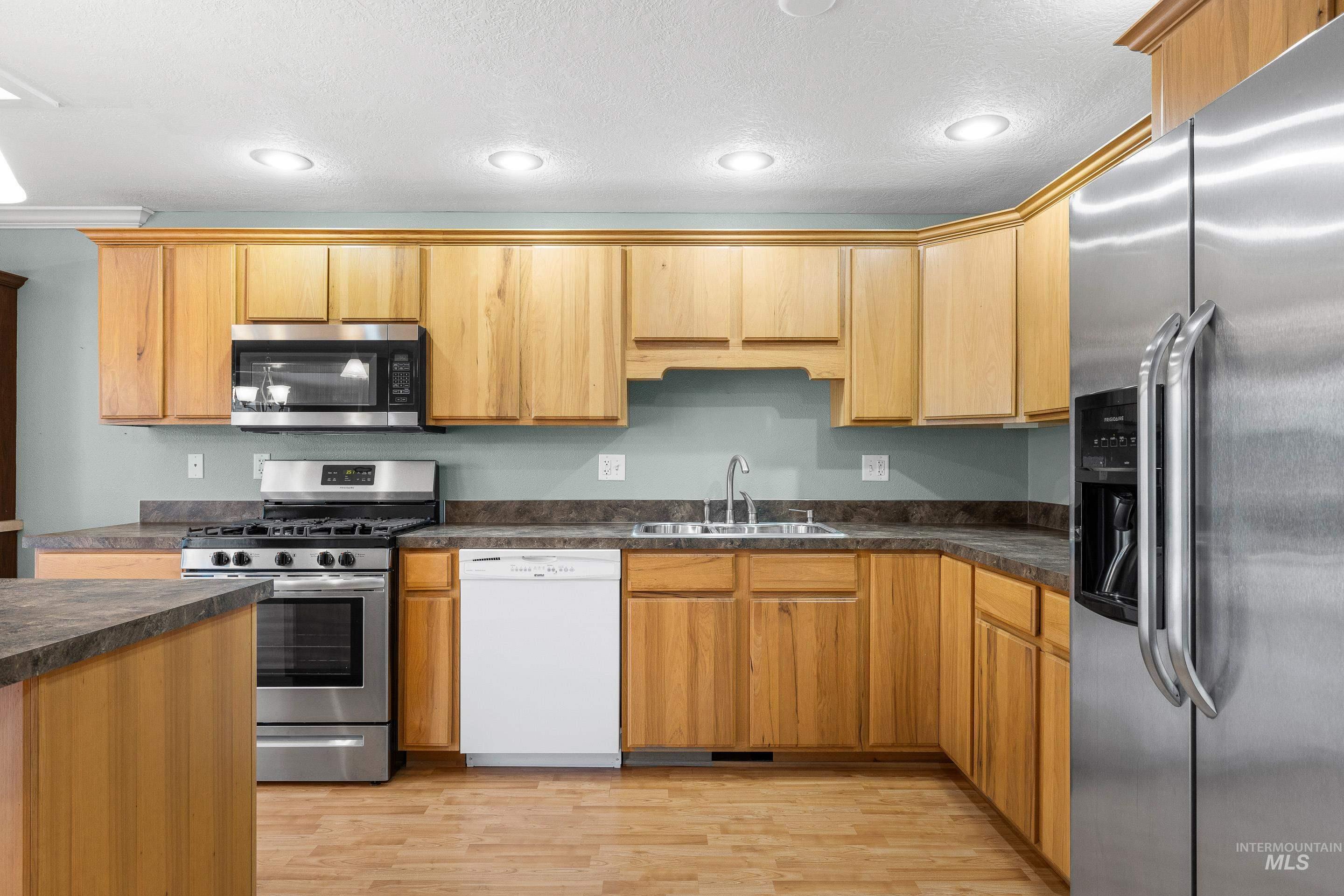 Kitchen featuring stainless steel appliances, dark countertops, light wood-type flooring, and recessed lighting