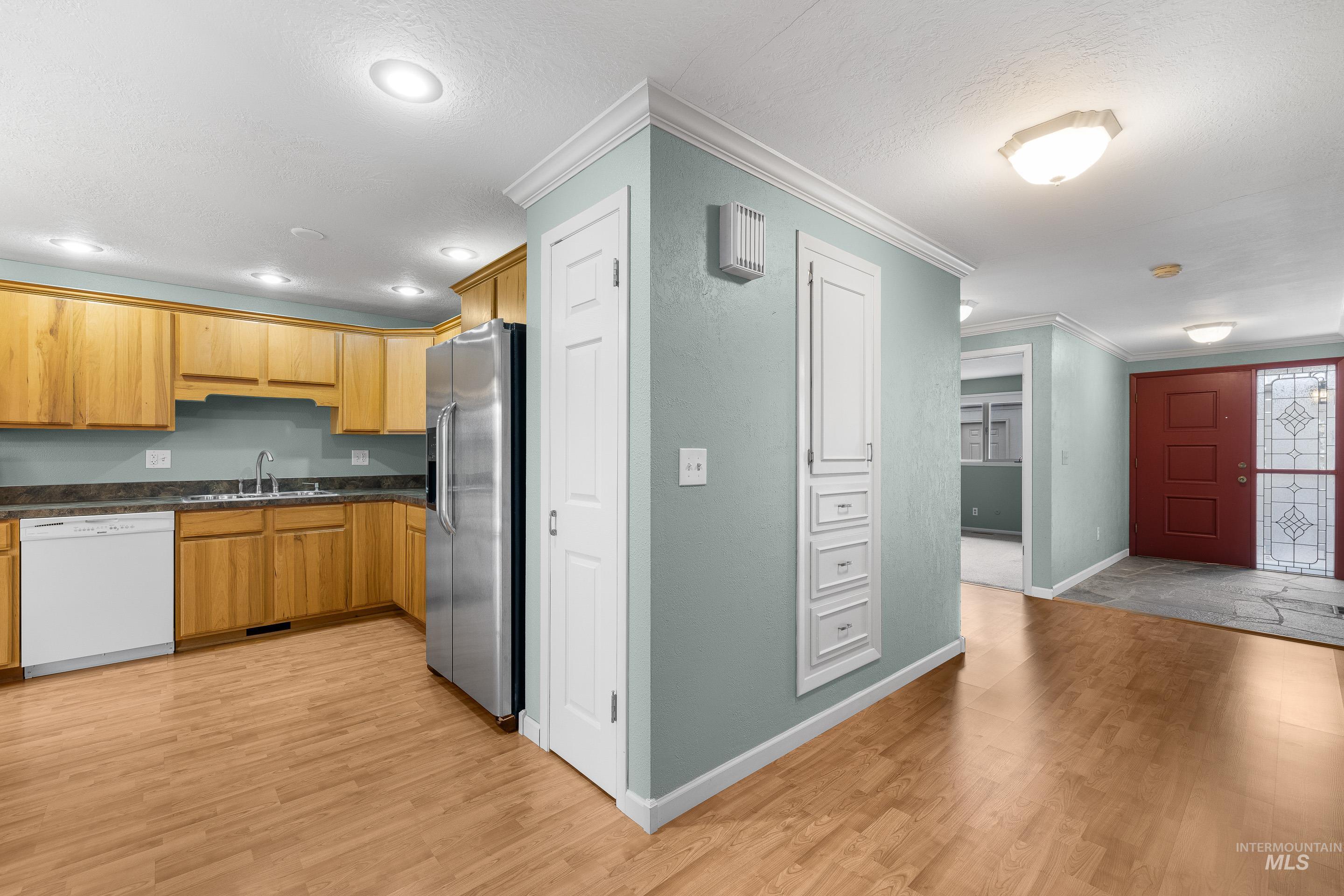 Kitchen featuring white dishwasher, stainless steel fridge with ice dispenser, light wood-style floors, ornamental molding, and wood finish cabinetry