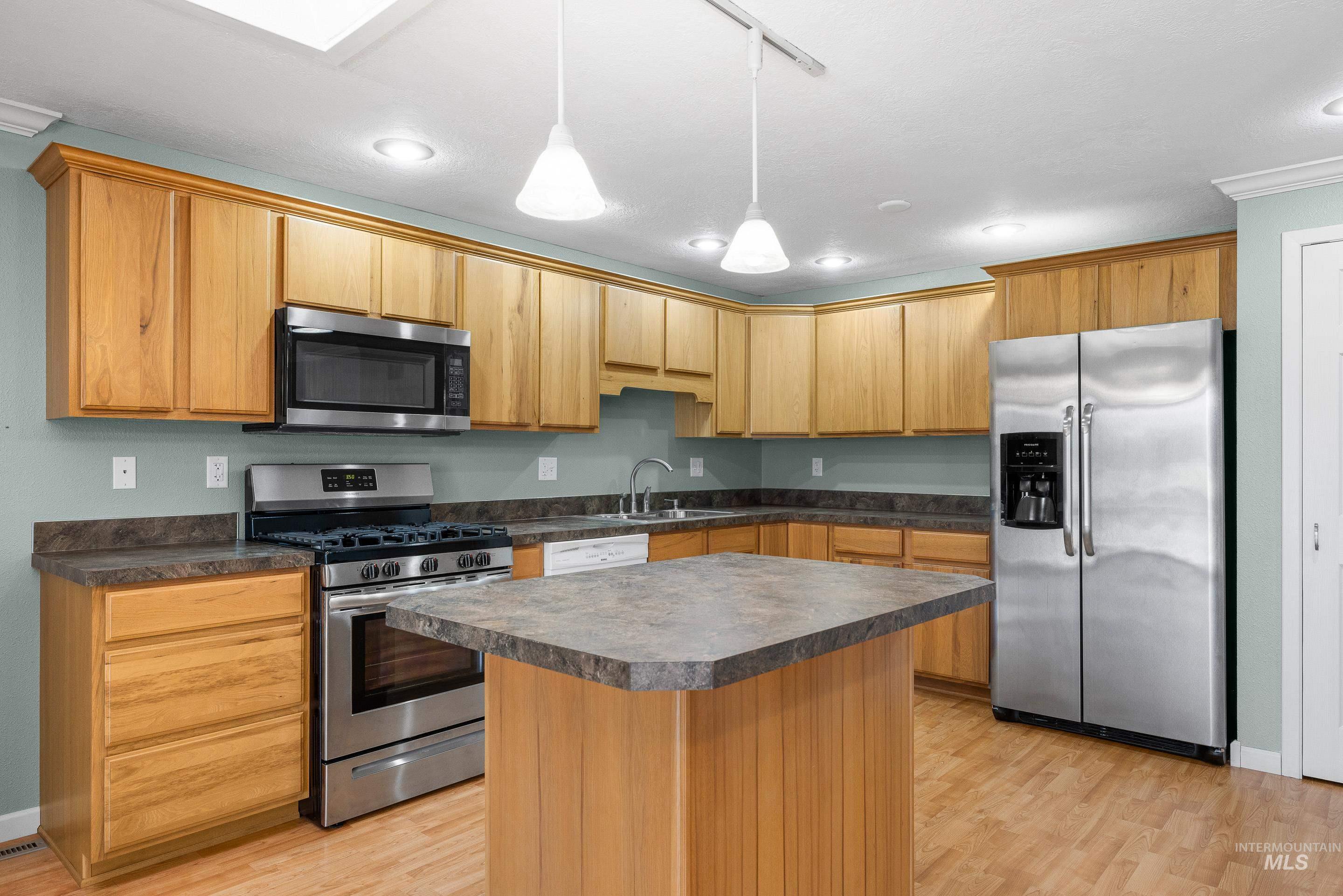 Kitchen featuring stainless steel appliances, dark countertops, decorative light fixtures, a center island, and light wood-type flooring