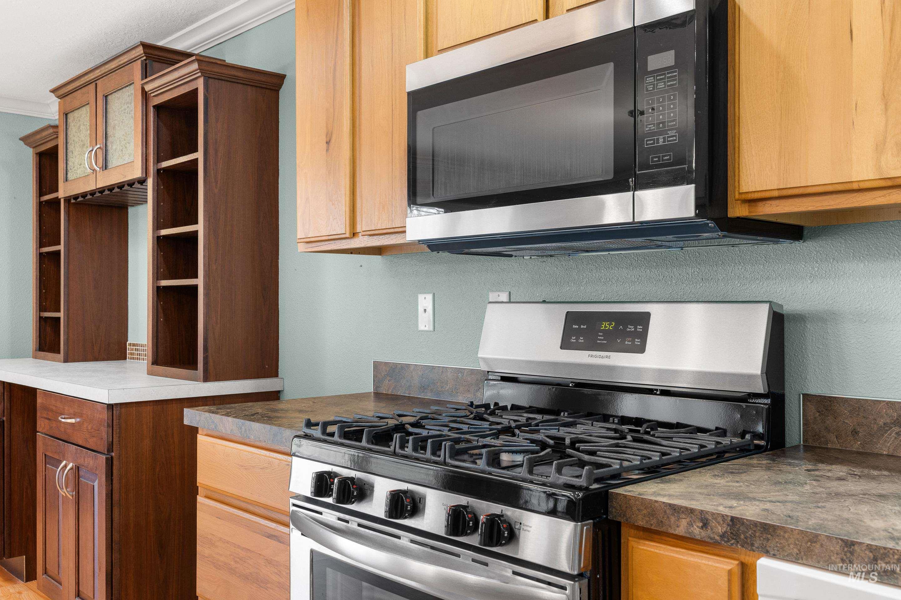 Kitchen with stainless steel appliances, ornamental molding, dark countertops, and open shelves