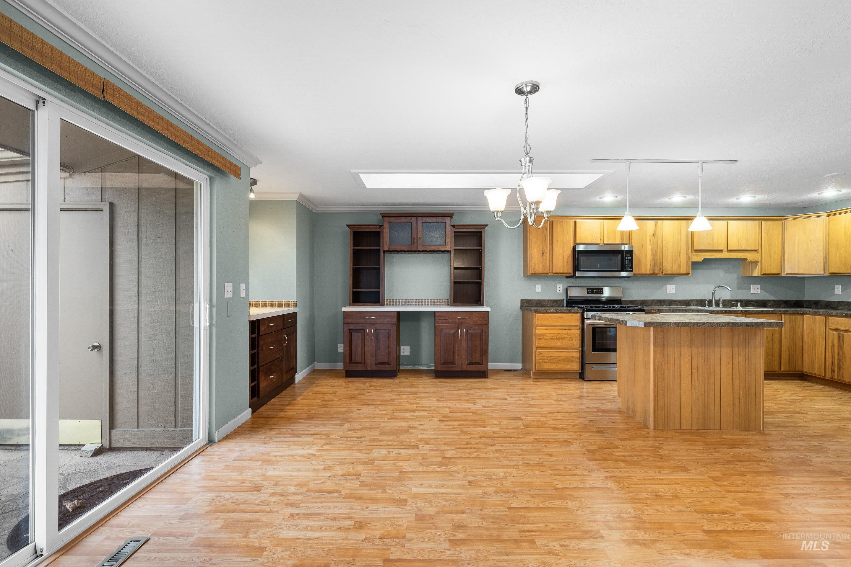 Kitchen with a center island, stainless steel appliances, suspended lighting, light wood-style flooring, and ornamental molding