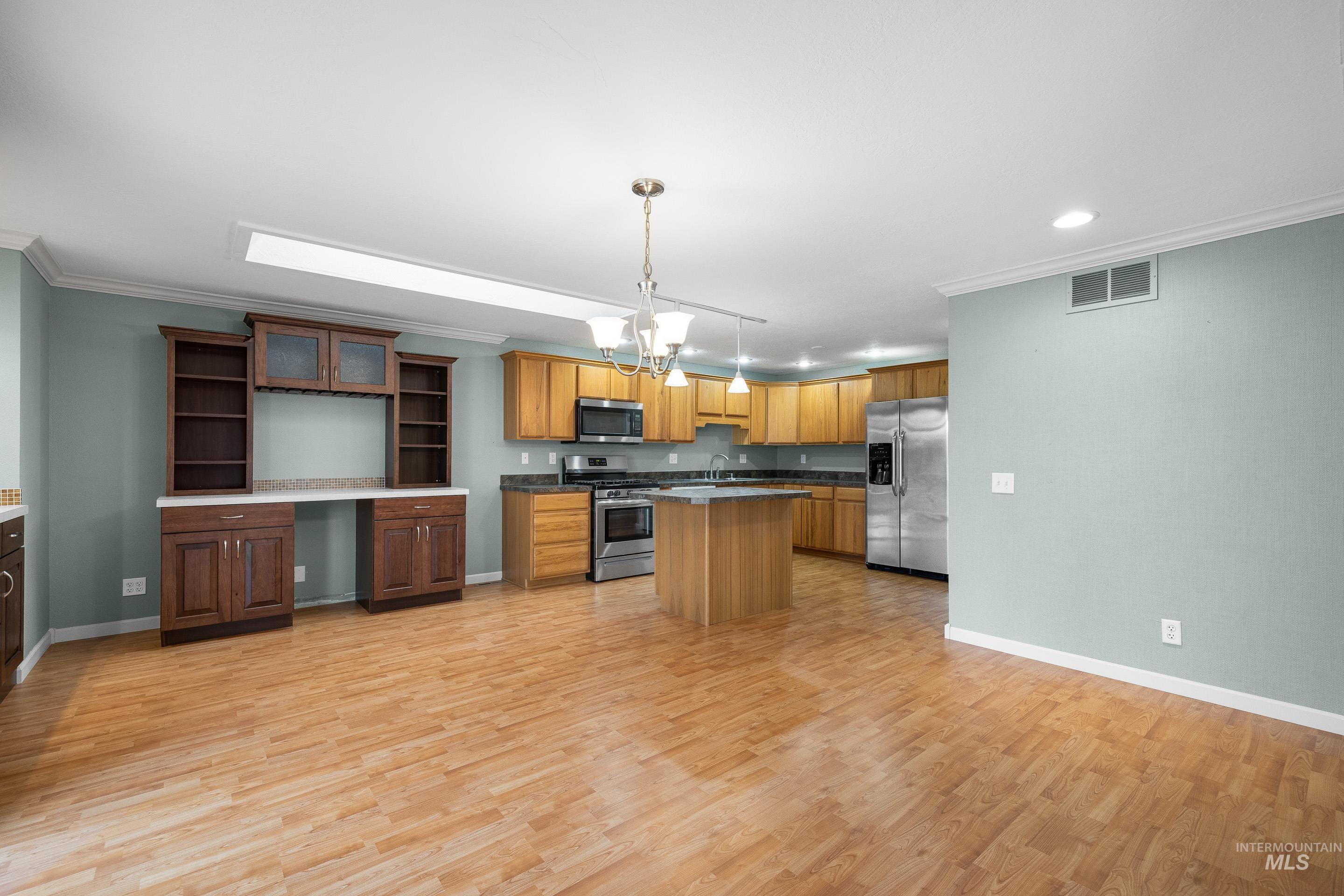 Kitchen featuring hanging lights, a kitchen island, stainless steel appliances, ornamental molding, and light wood-style flooring