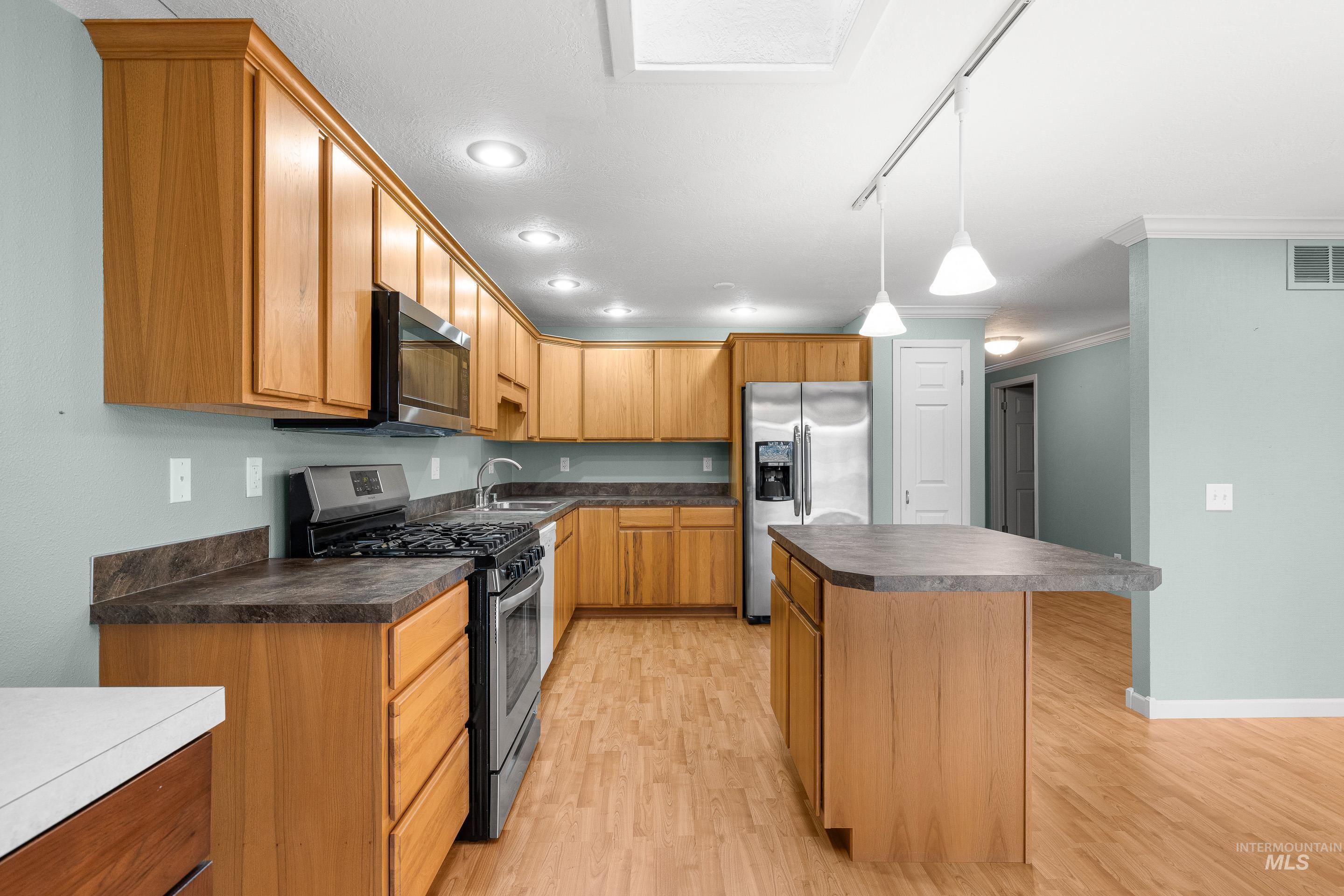 Kitchen with dark countertops, stainless steel appliances, a kitchen island, decorative light fixtures, and light wood-type flooring