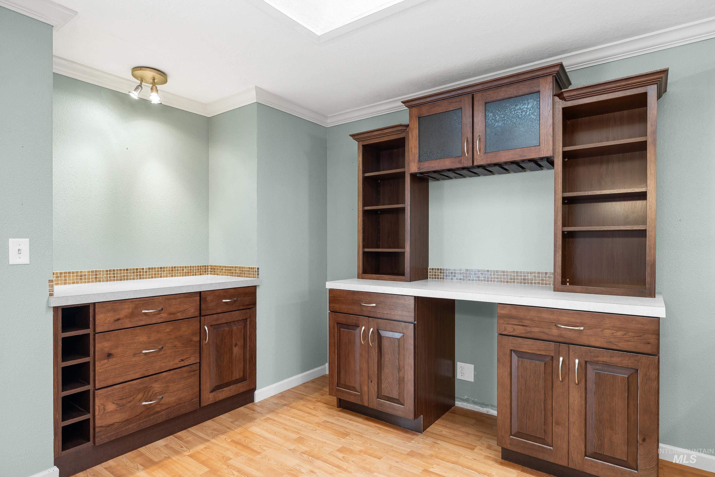 Bar featuring built in study area, light wood-style flooring, light countertops, crown molding, and open shelves
