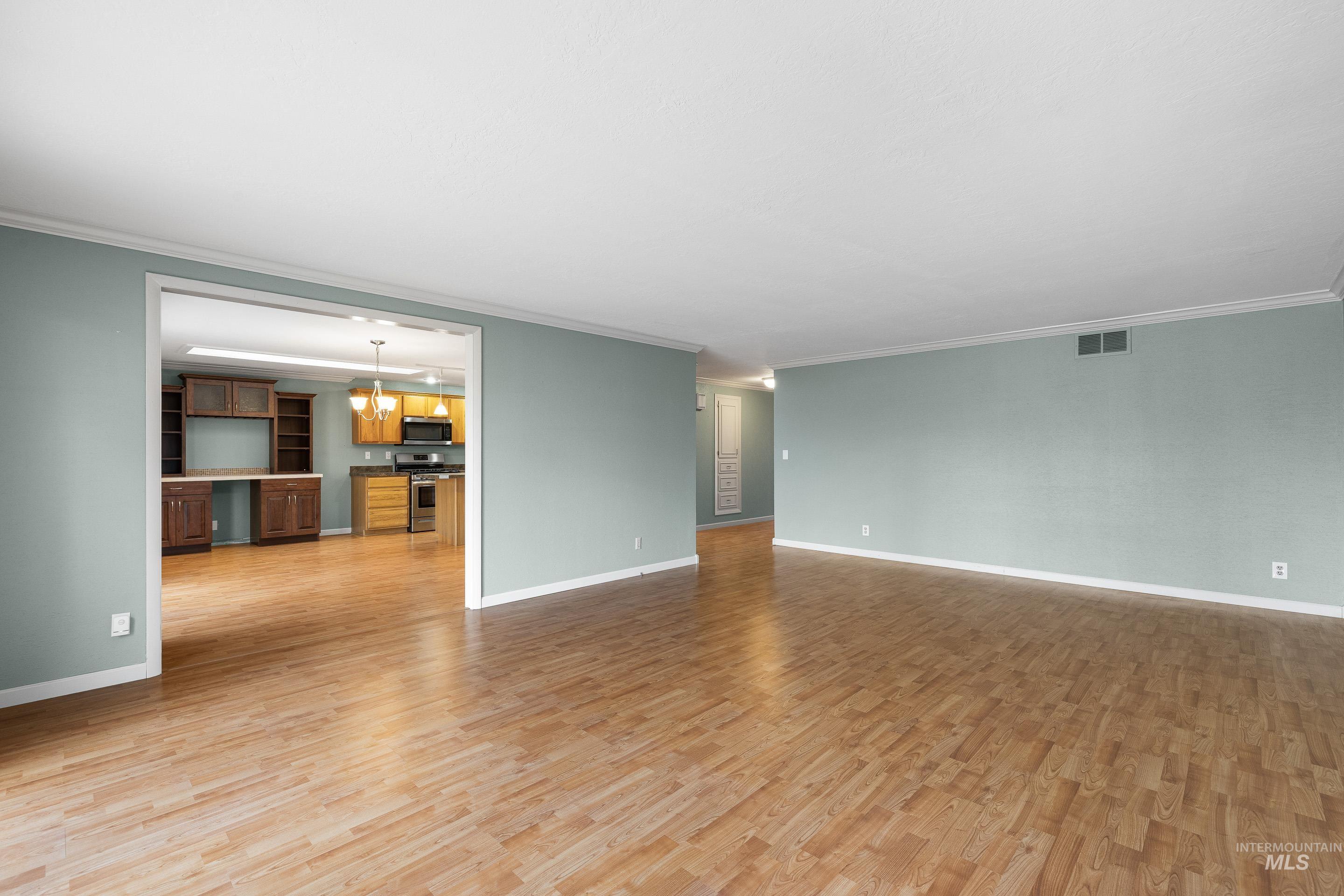 Unfurnished living room with light wood-style flooring and crown molding