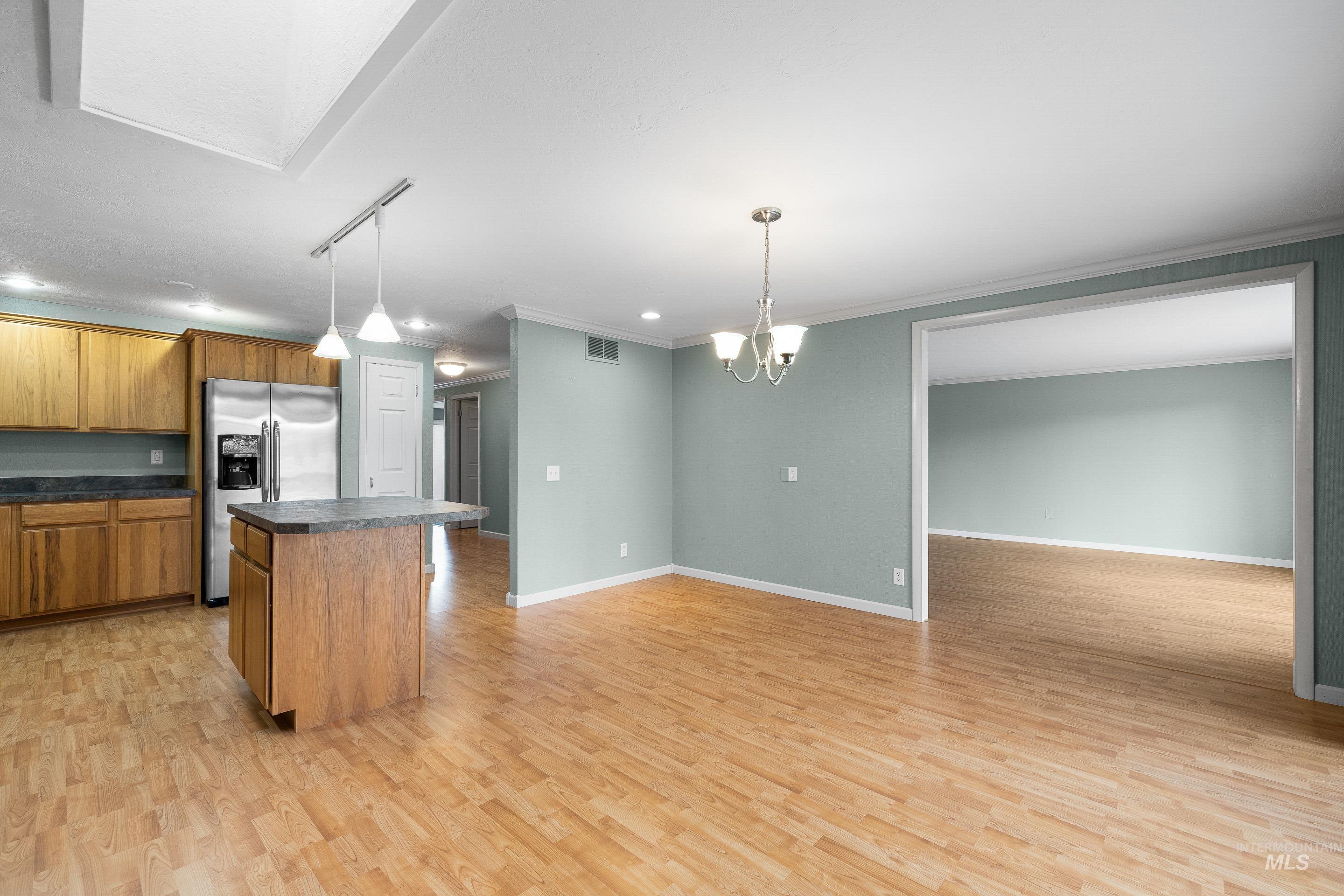 Kitchen with dark countertops, wood finish cabinets, a center island, suspended lighting, and light wood finished floors