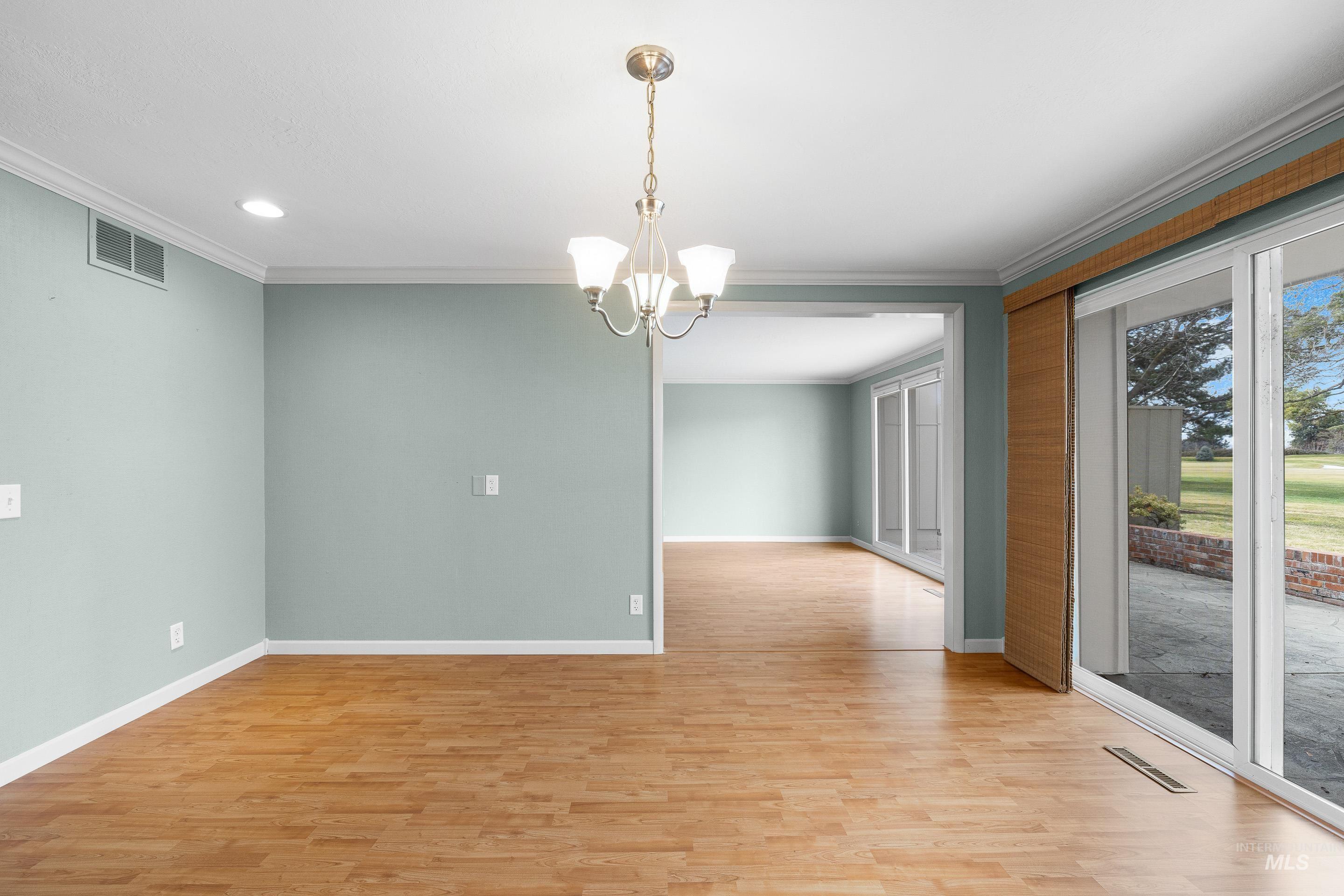 Spare room with hanging lights, light wood-style flooring, and crown molding