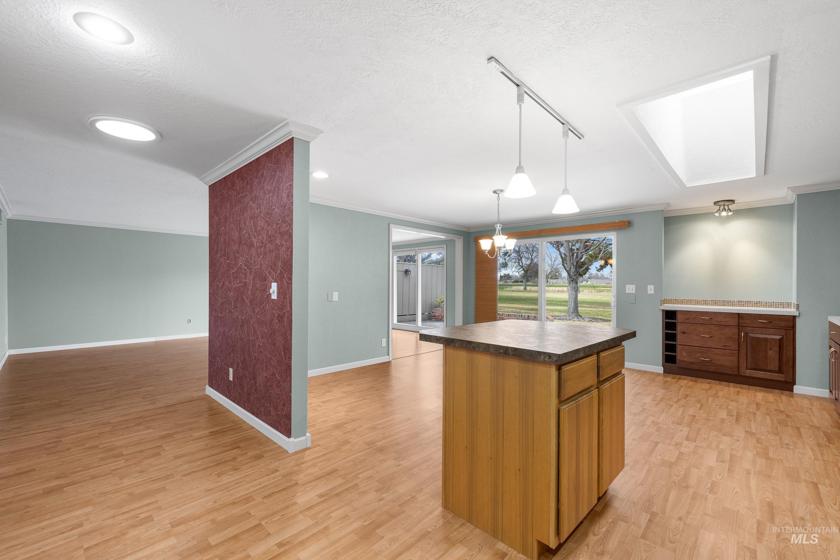 Kitchen featuring a center island, a skylight, light wood finished floors, dark countertops, and ornamental molding