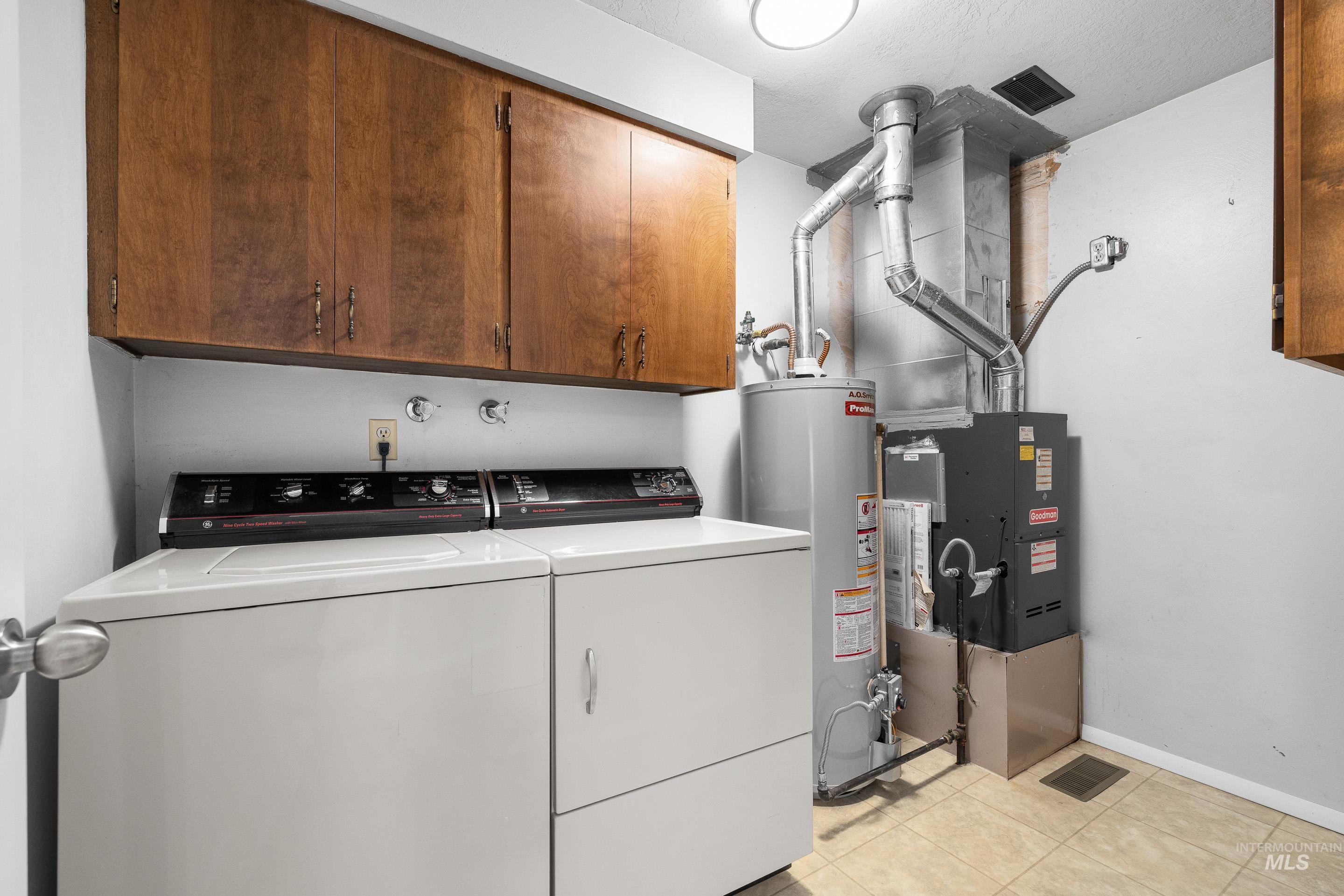 Laundry room with cabinet space, water heater, independent washer and dryer, heating unit, and light tile patterned floors