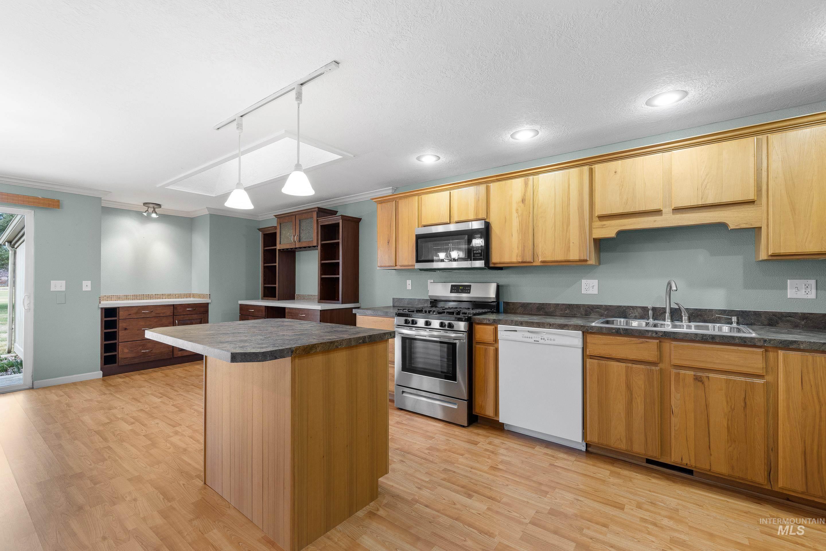 Kitchen featuring track lighting, stainless steel appliances, a center island, light wood-style flooring, and dark countertops