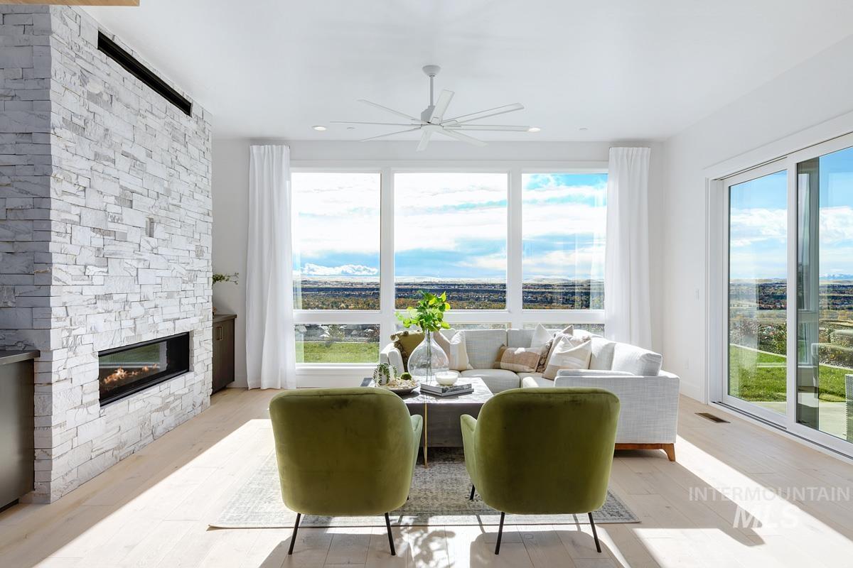 Living room featuring light wood-type flooring, healthy amount of natural light, a stone fireplace, and ceiling fan