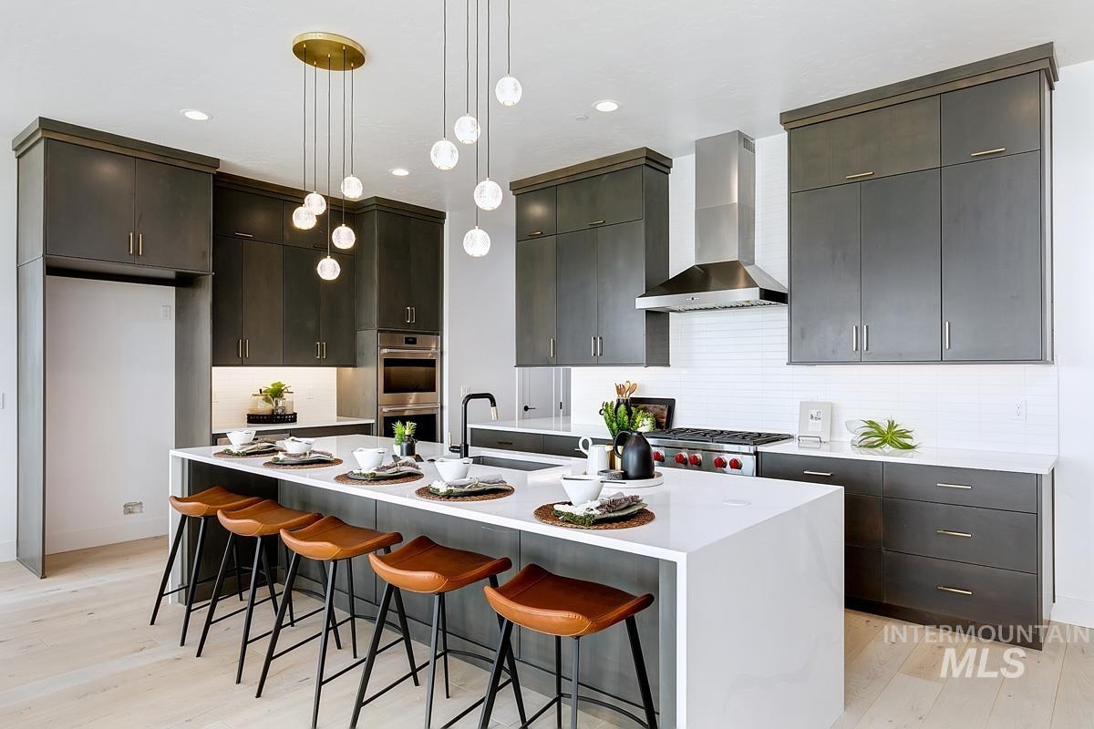 Kitchen featuring a kitchen bar, backsplash, pendant lighting, wall chimney exhaust hood, and light wood-type flooring