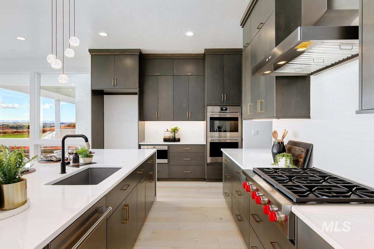 Kitchen with wall chimney exhaust hood, hanging light fixtures, appliances with stainless steel finishes, recessed lighting, and tasteful backsplash