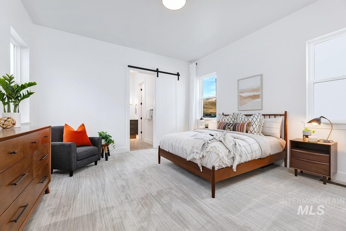 Bedroom featuring a barn door, light colored carpet, and connected bathroom