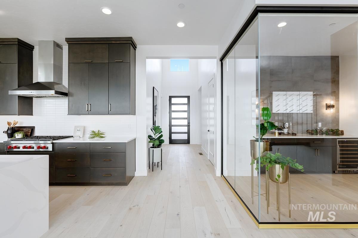 Kitchen featuring wall chimney range hood, light wood-style flooring, modern cabinets, beverage cooler, and tasteful backsplash