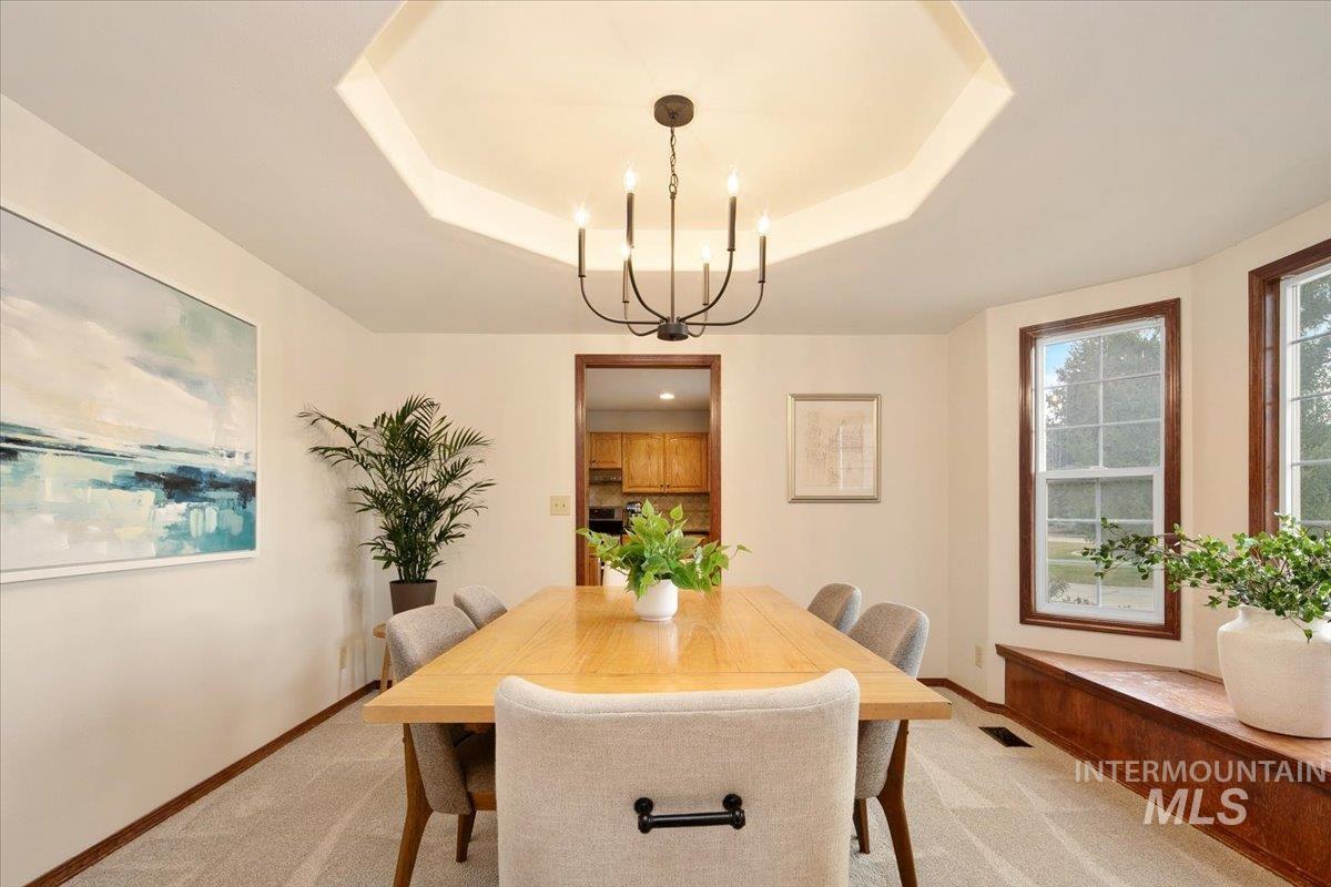 Dining space featuring light carpet, a chandelier, and a raised ceiling